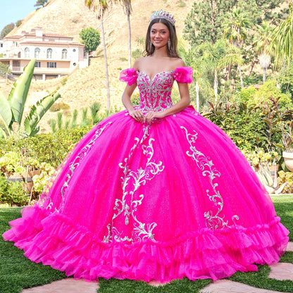Woman in a fuchsia pink quinceañera dress with white embroidery standing outdoors.