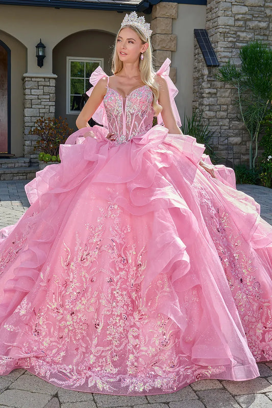 Woman in a pink quinceañera dress with floral details and a tiara, standing in front of a stone building.