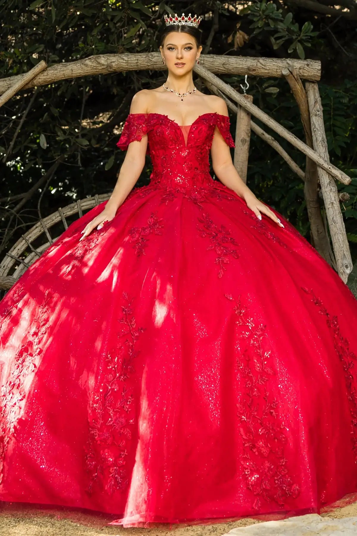 Woman in a red ball gown with floral embroidery sitting outdoors.
