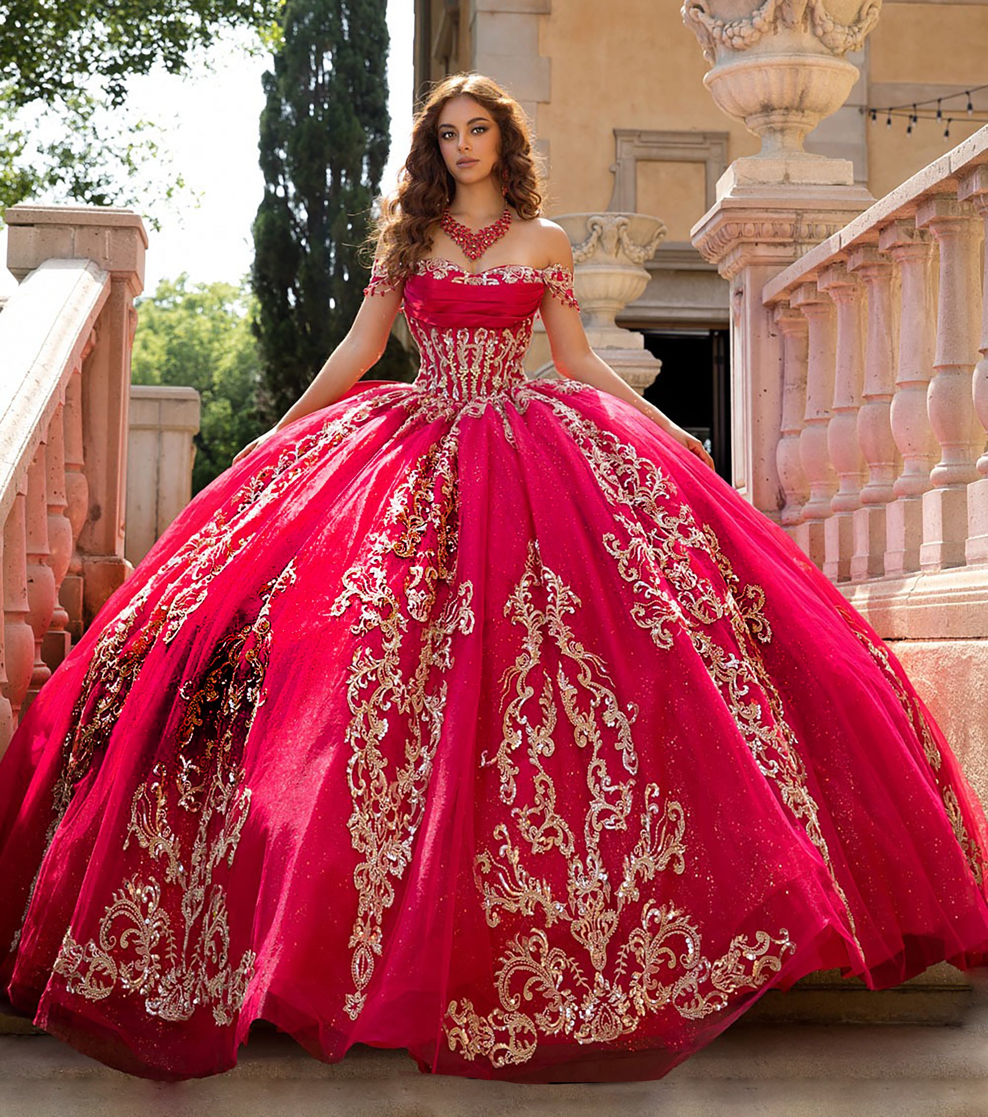 Woman in a red and gold quinceañera dress standing outdoors.