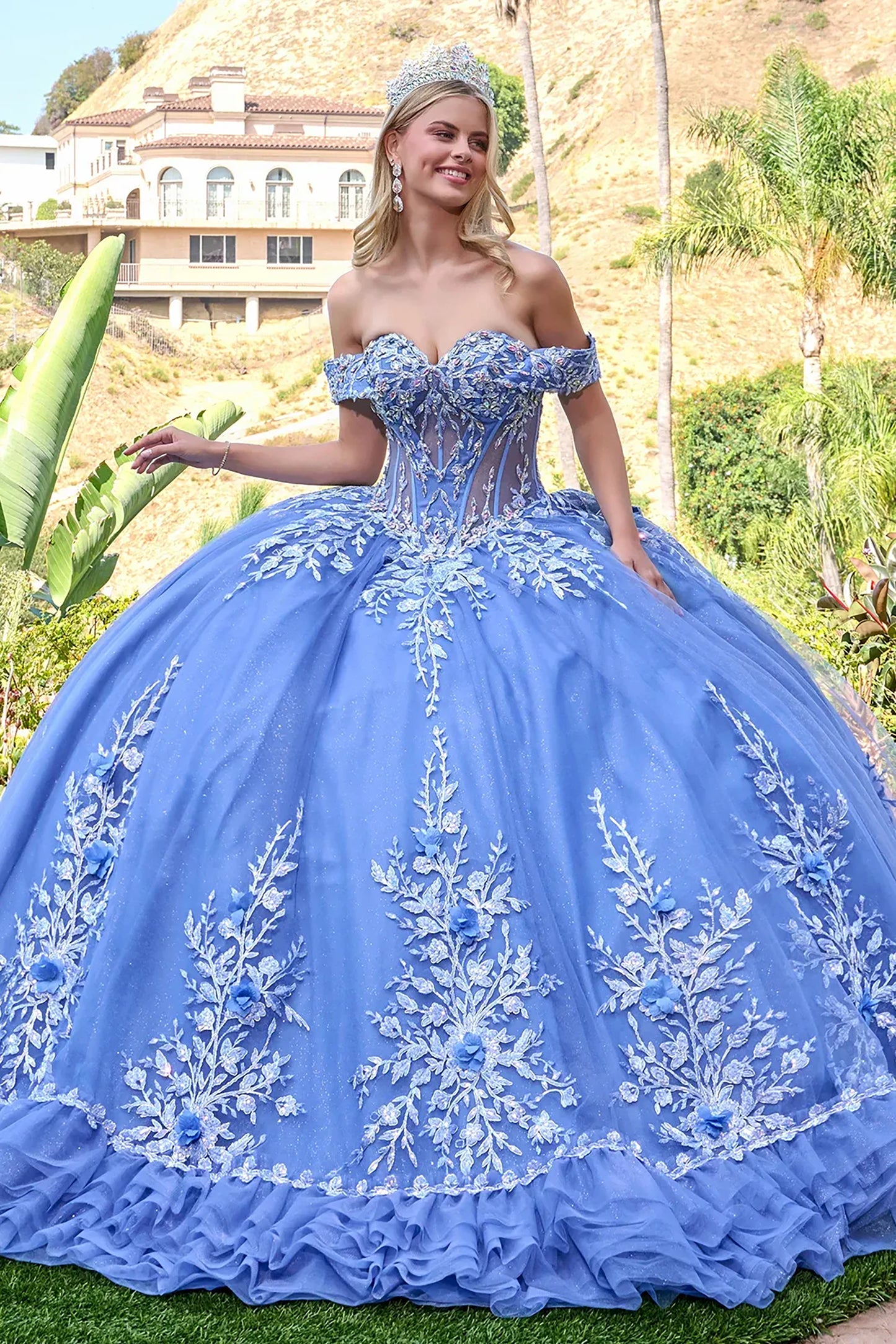 Woman in a dusty blue quince  embroidered ball gown standing outdoors with greenery and a house in the background.