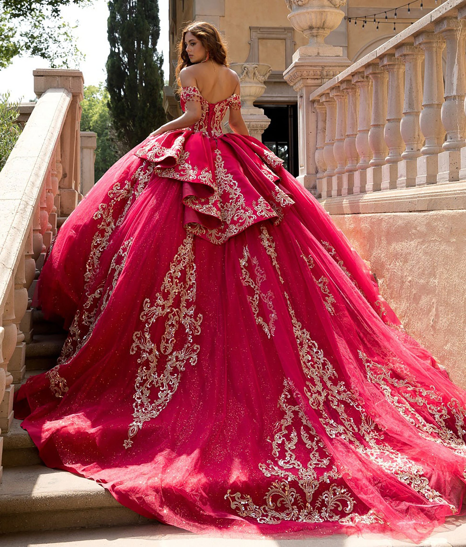 Woman in a red ball gown with gold embroidery standing on stone steps.