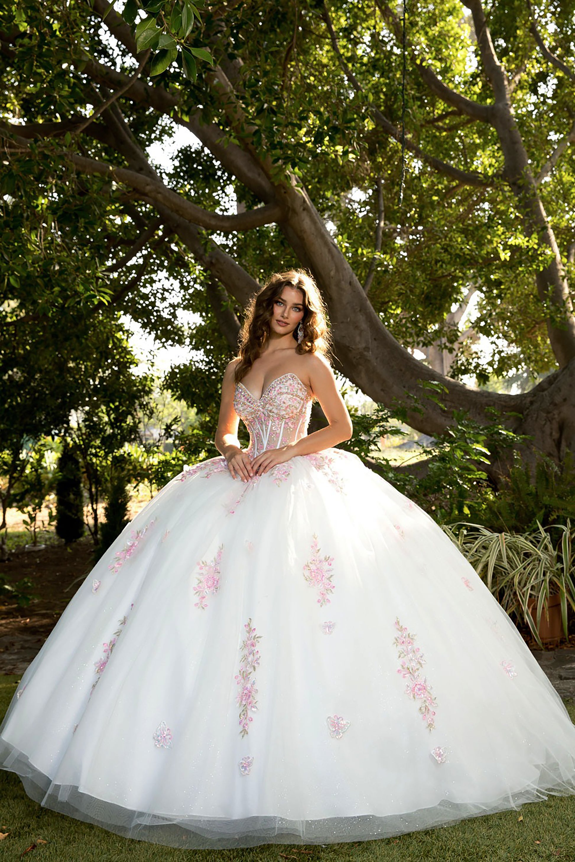 Woman in a white ballgown with floral details standing under a tree