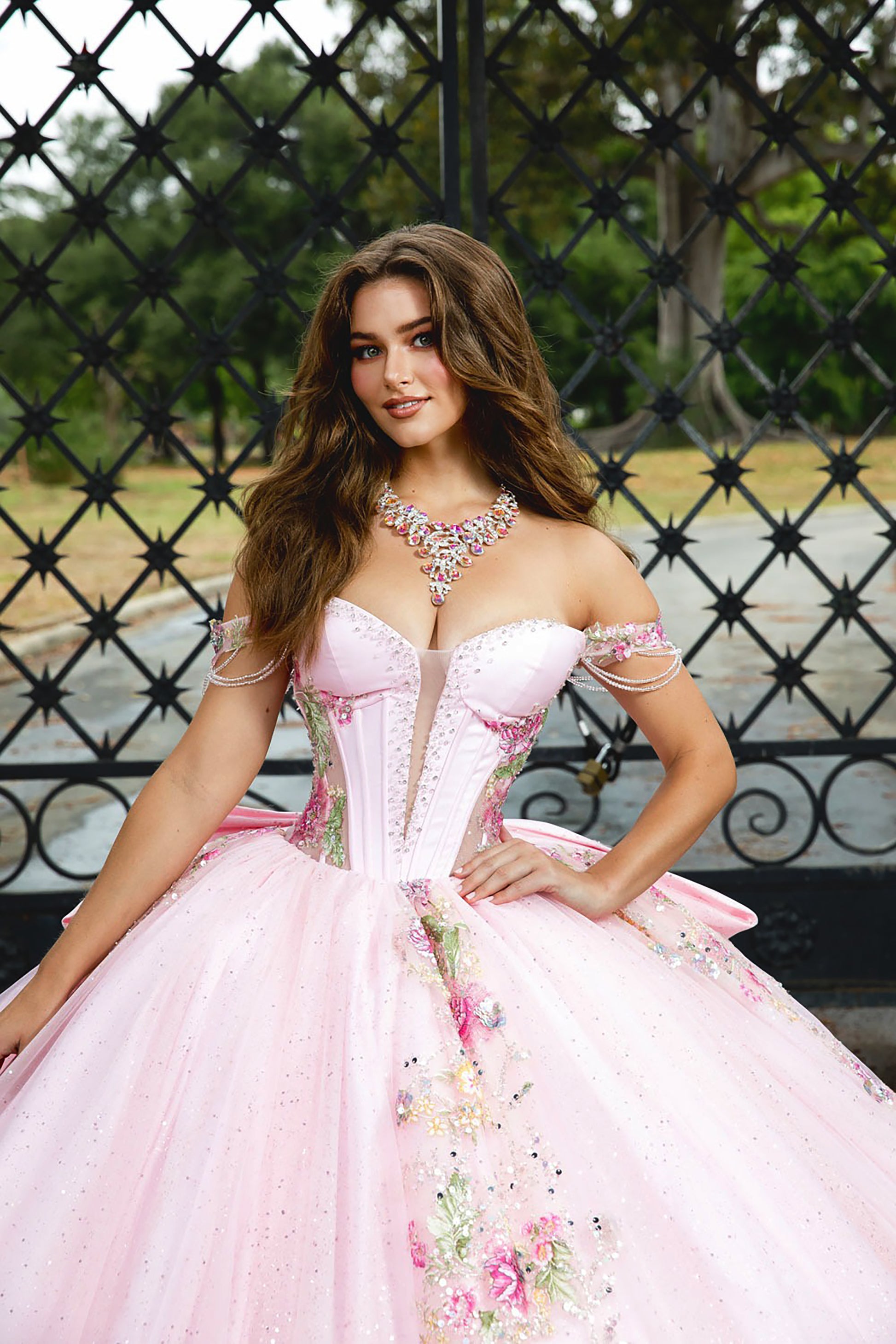 Woman in a pink formal gown with floral details sitting outdoors.