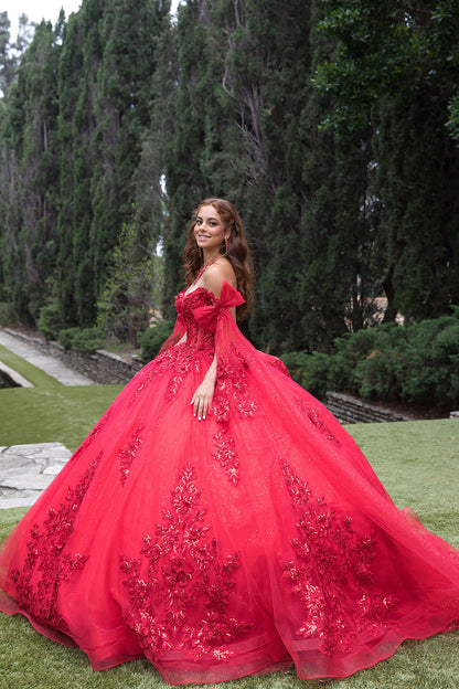 Woman in a red ball gown standing outdoors with greenery in the background