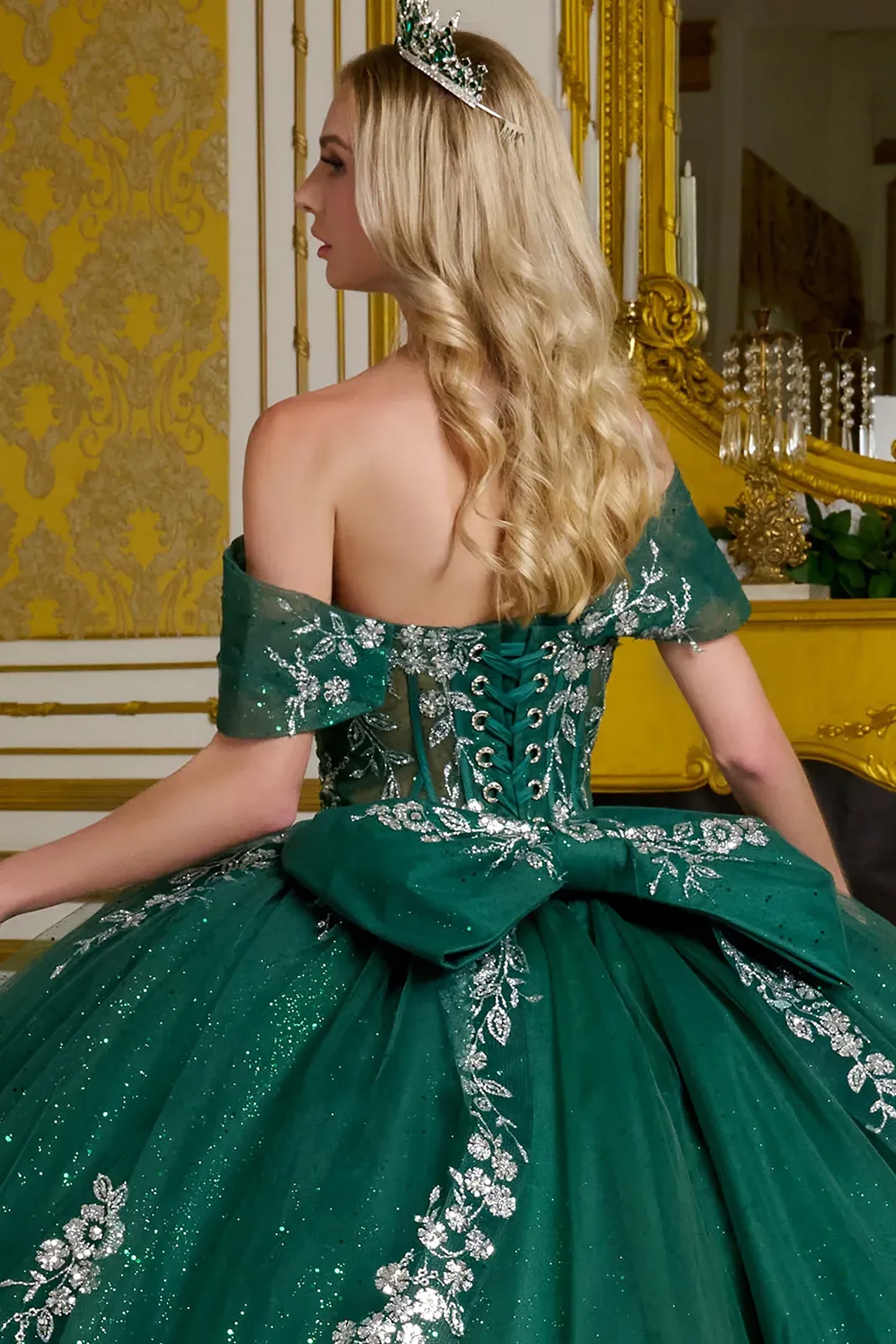 Woman in a green gown with floral details sitting in a decorated room.