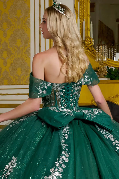 Woman in a green gown with floral details sitting in a decorated room.