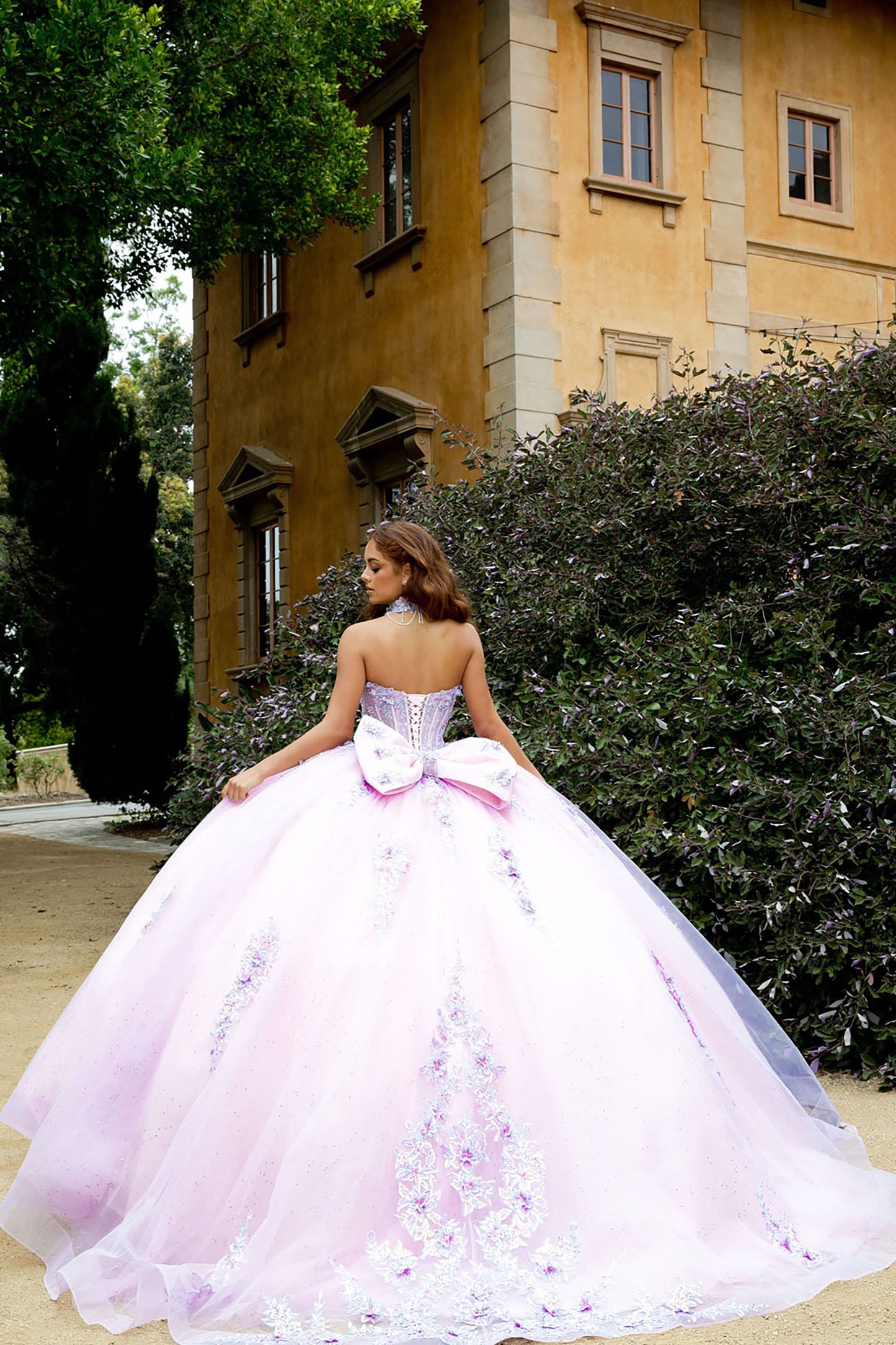 Woman in a pink and white floral gown standing in front of a building with greenery.