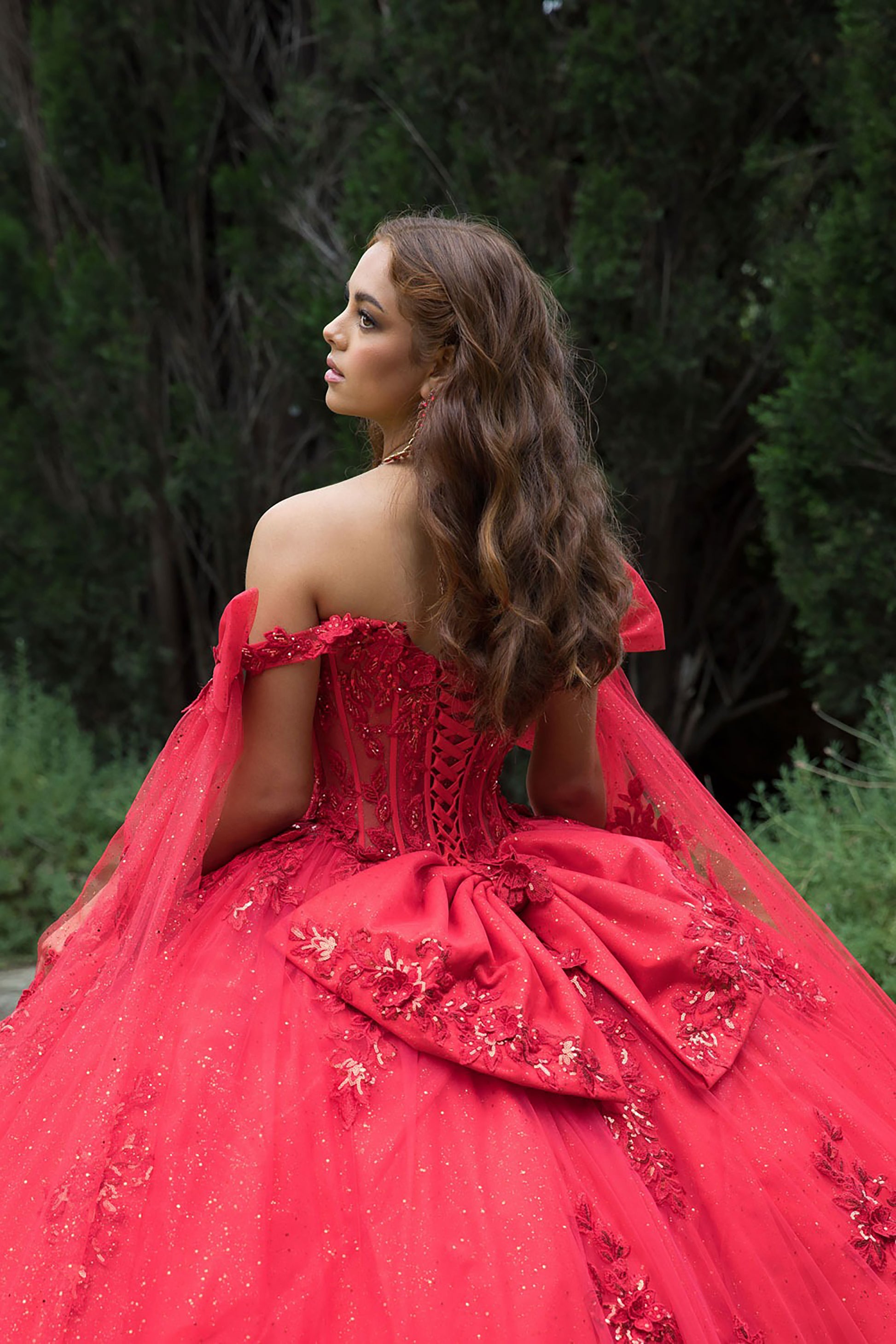 Woman in a red, ornate dress standing outdoors with greenery in the background