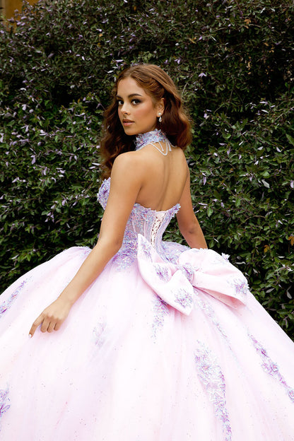 Woman in a pink and white formal gown with a floral headpiece against a green bush background