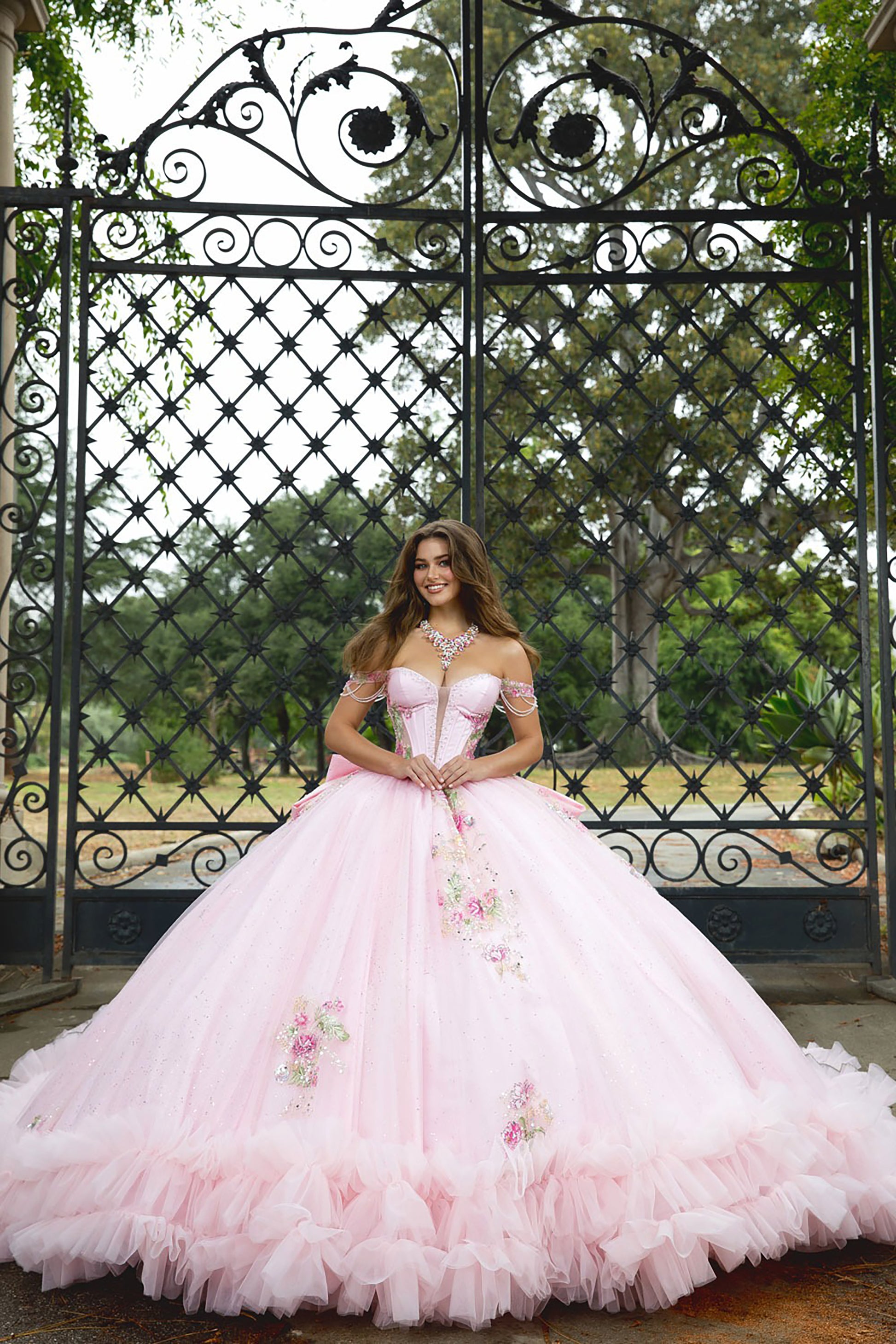 Woman in a pink ball gown standing in front of an ornate metal gate.