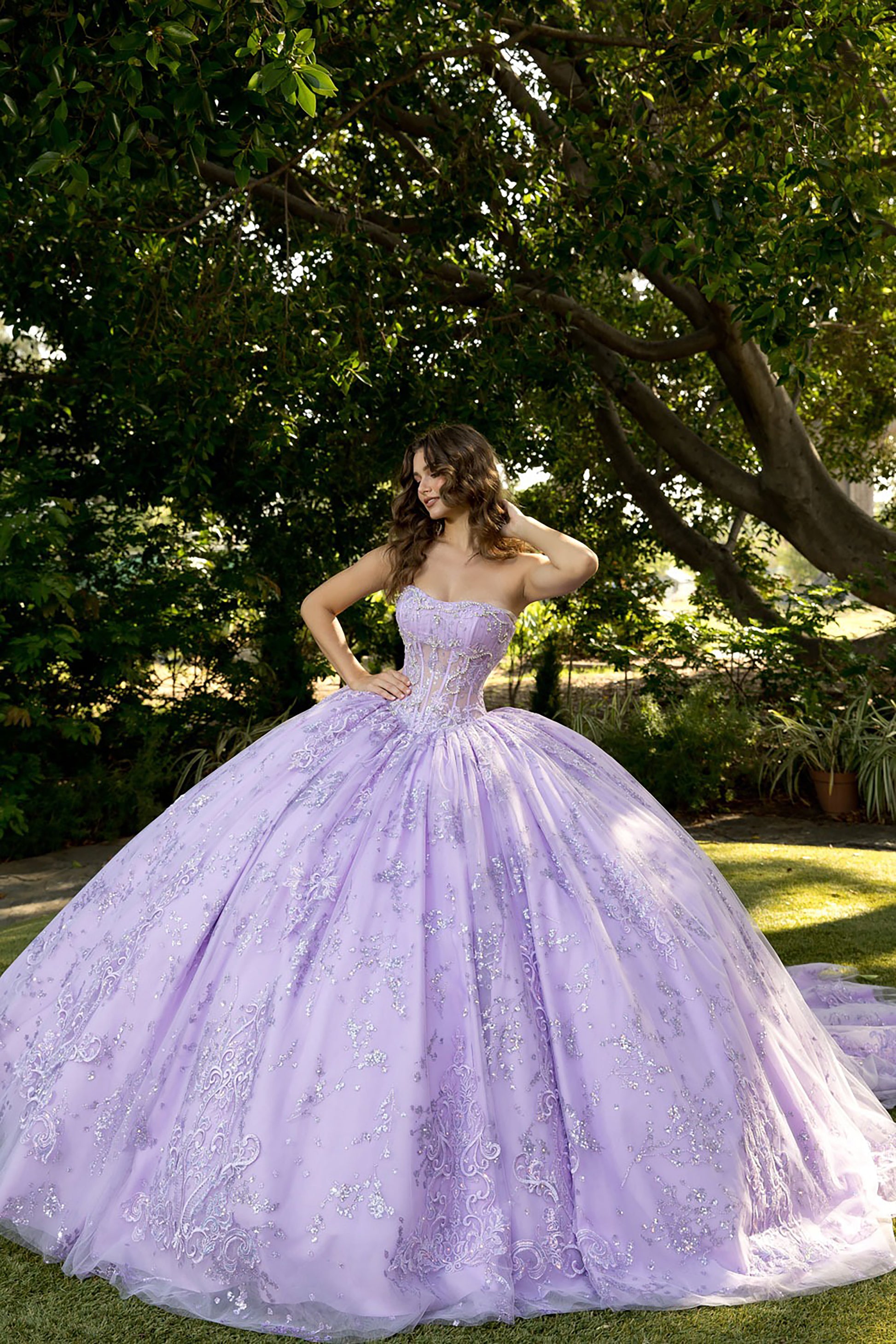 Woman in a lavender ball gown standing outdoors with trees and grass in the background