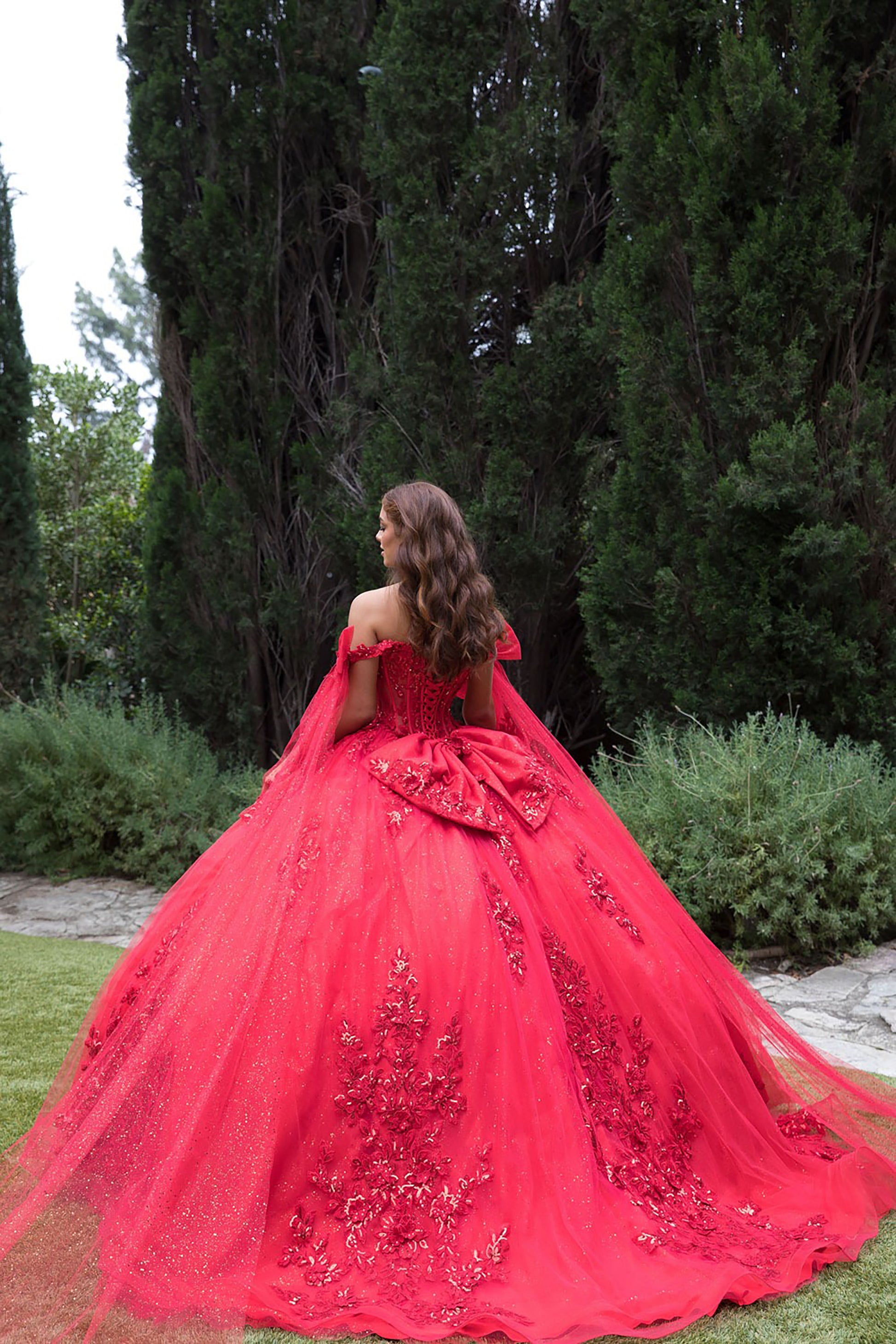 Woman in a red ball gown with floral details standing in a garden.