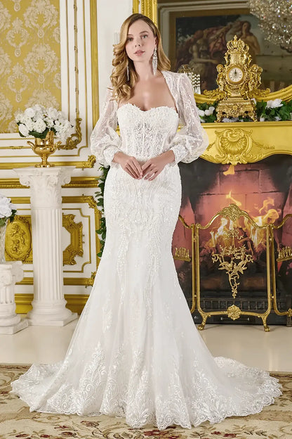 Woman in a white lace wedding dress  with long sleeve bolero standing in an ornate room with gold accents.