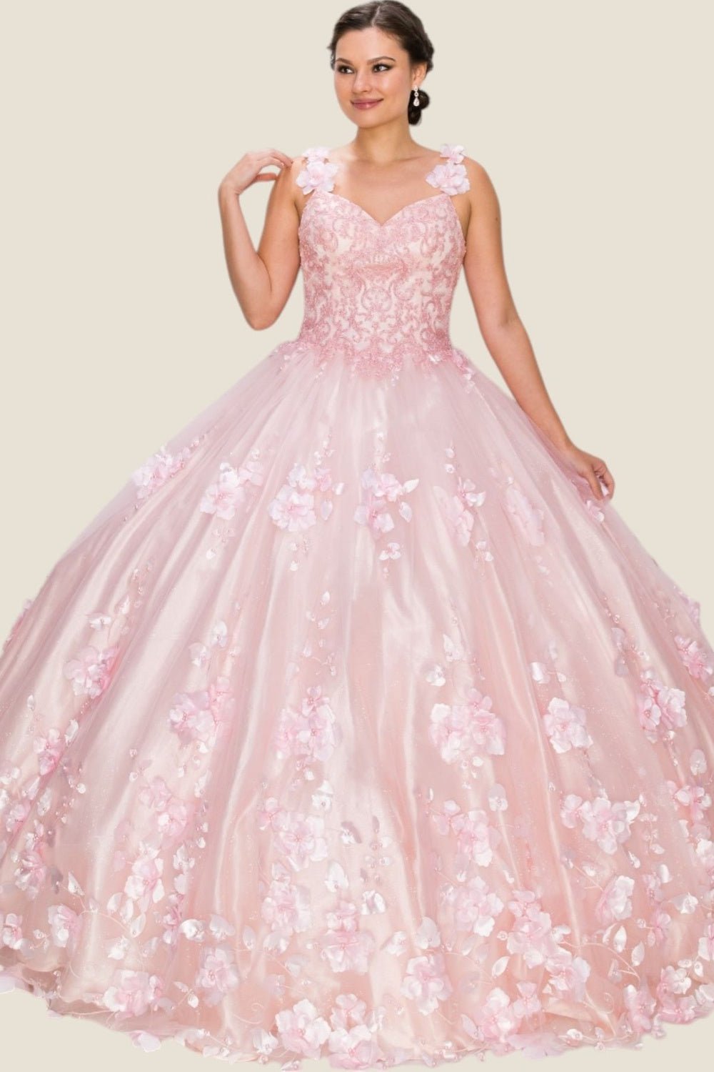 Woman standing front-facing in blush pink ball gown with floral lace appliqués, sweetheart neckline, wide straps, and voluminous layered skirt with floral embellishments