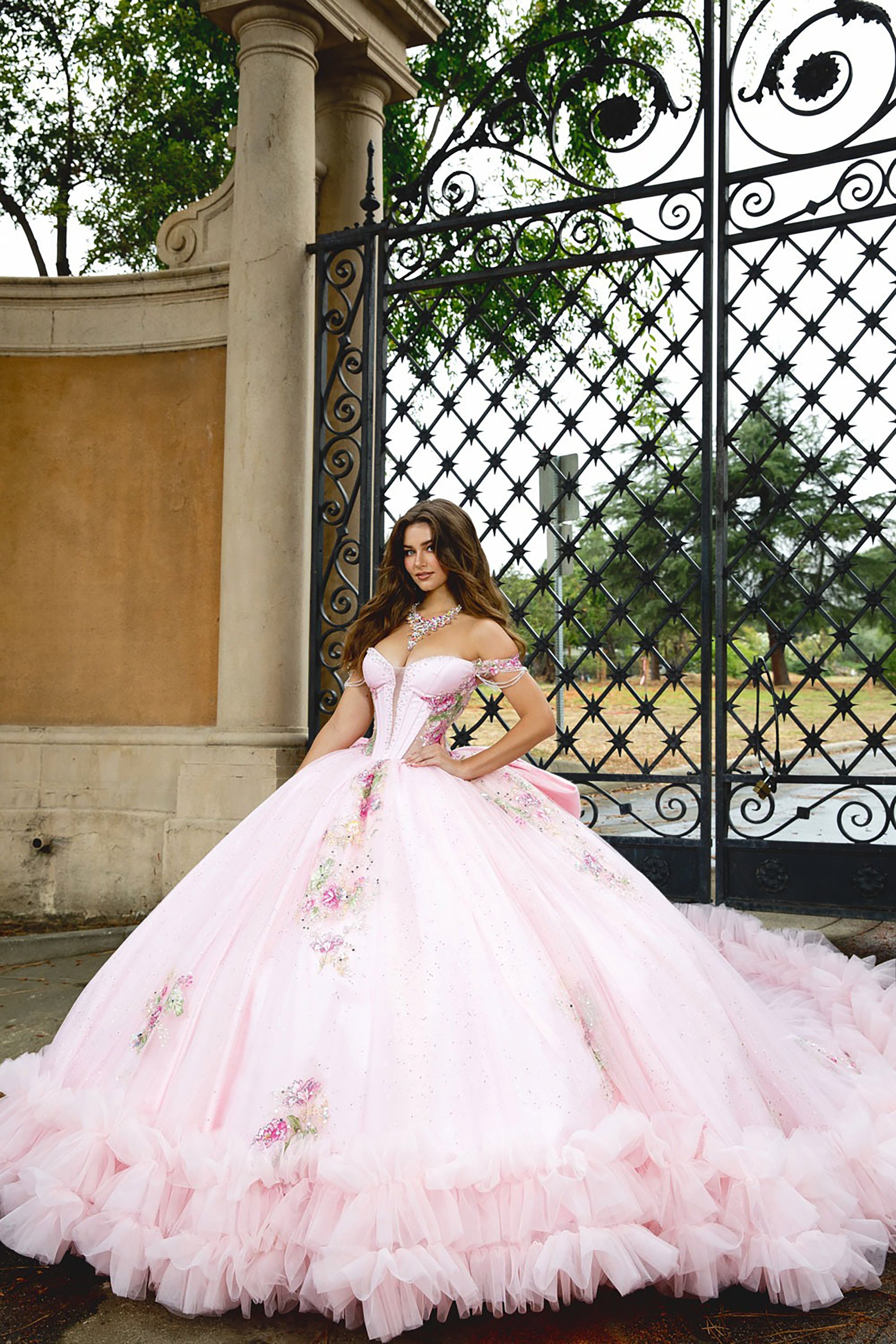 Woman in a pink floral dress standing in front of an ornate black gate.