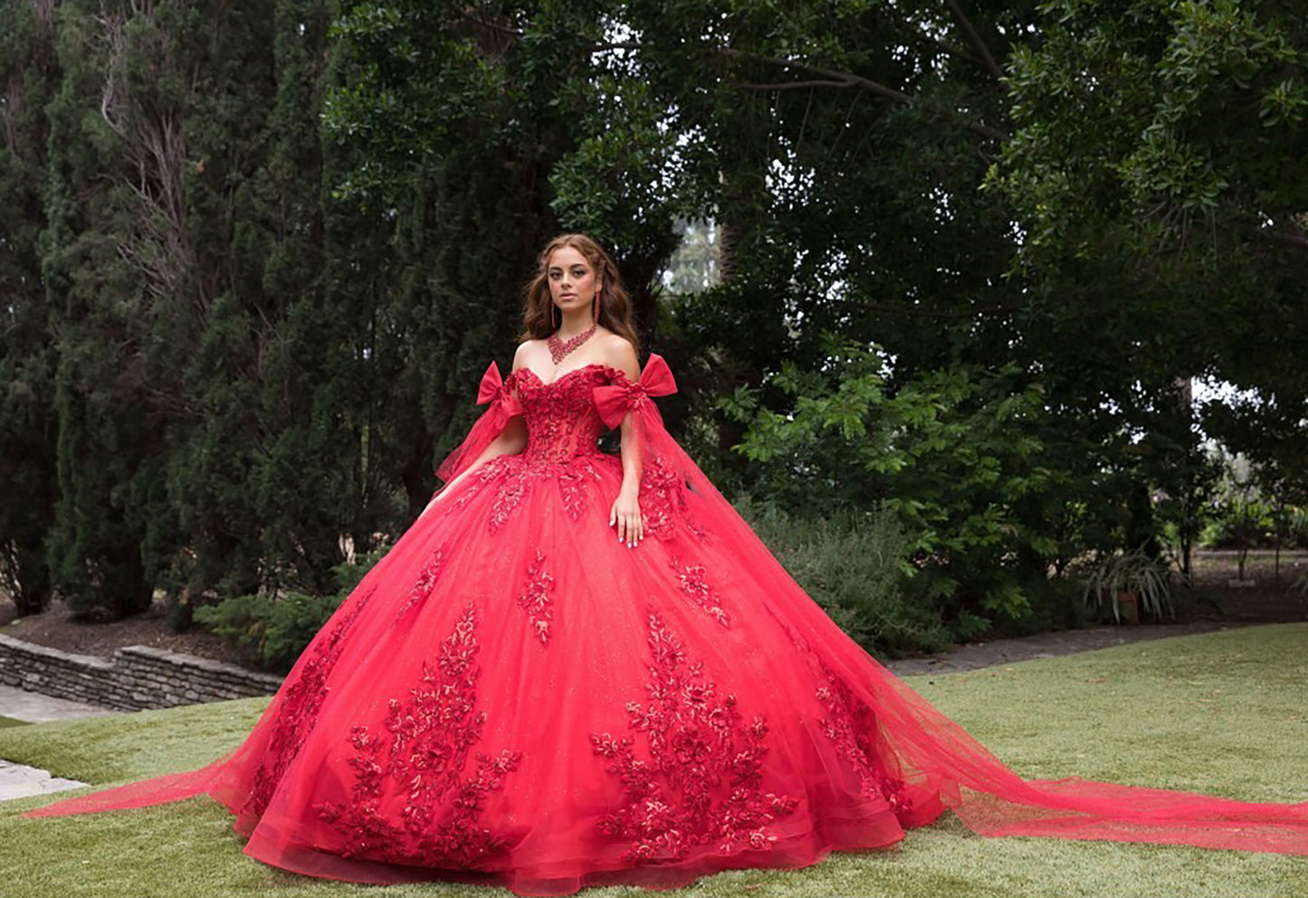 Woman in a red ball gown standing outdoors with trees in the background