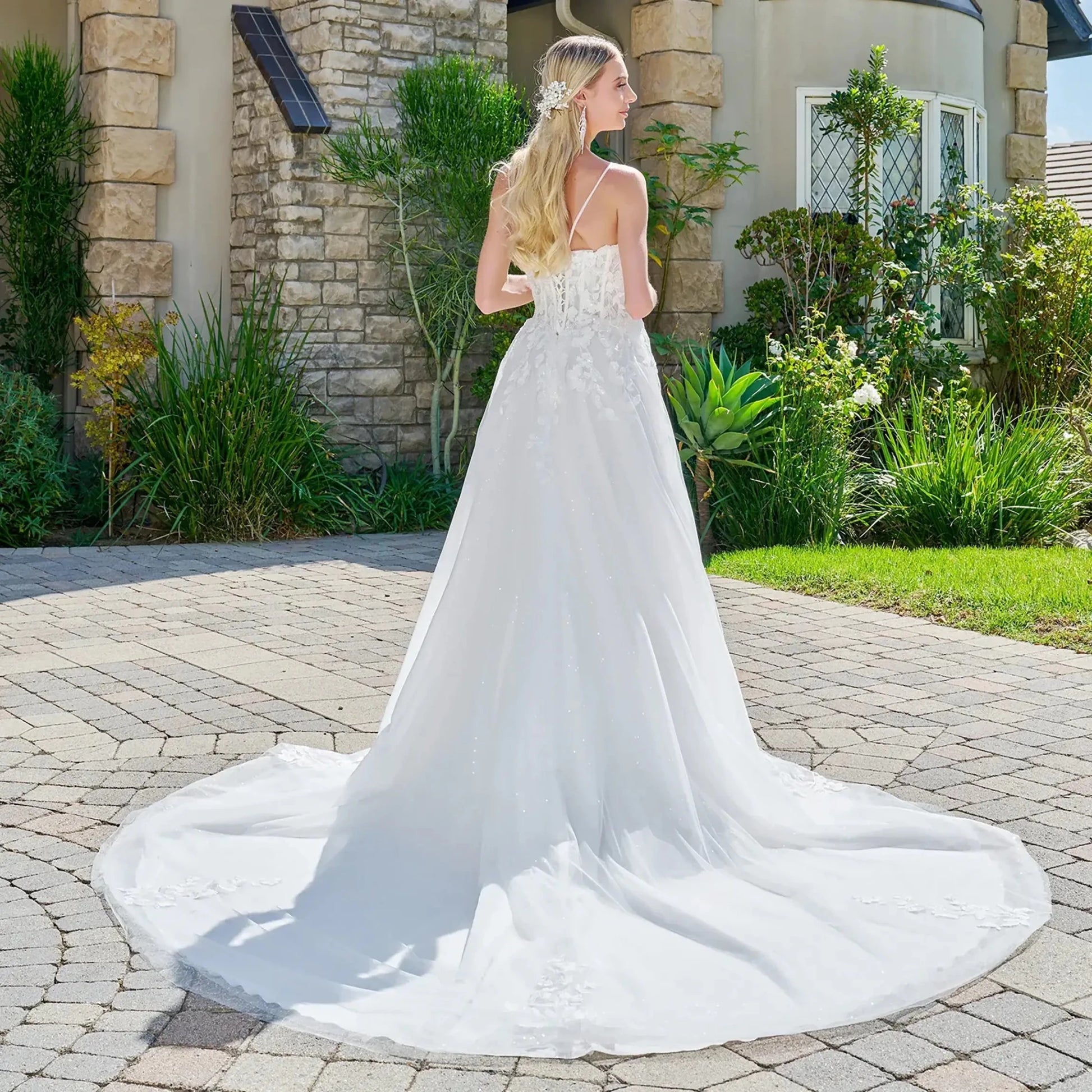 Woman in a white wedding dress standing on a driveway with a garden and house in the background