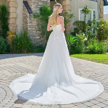 Woman in a white wedding dress standing on a driveway with a garden and house in the background