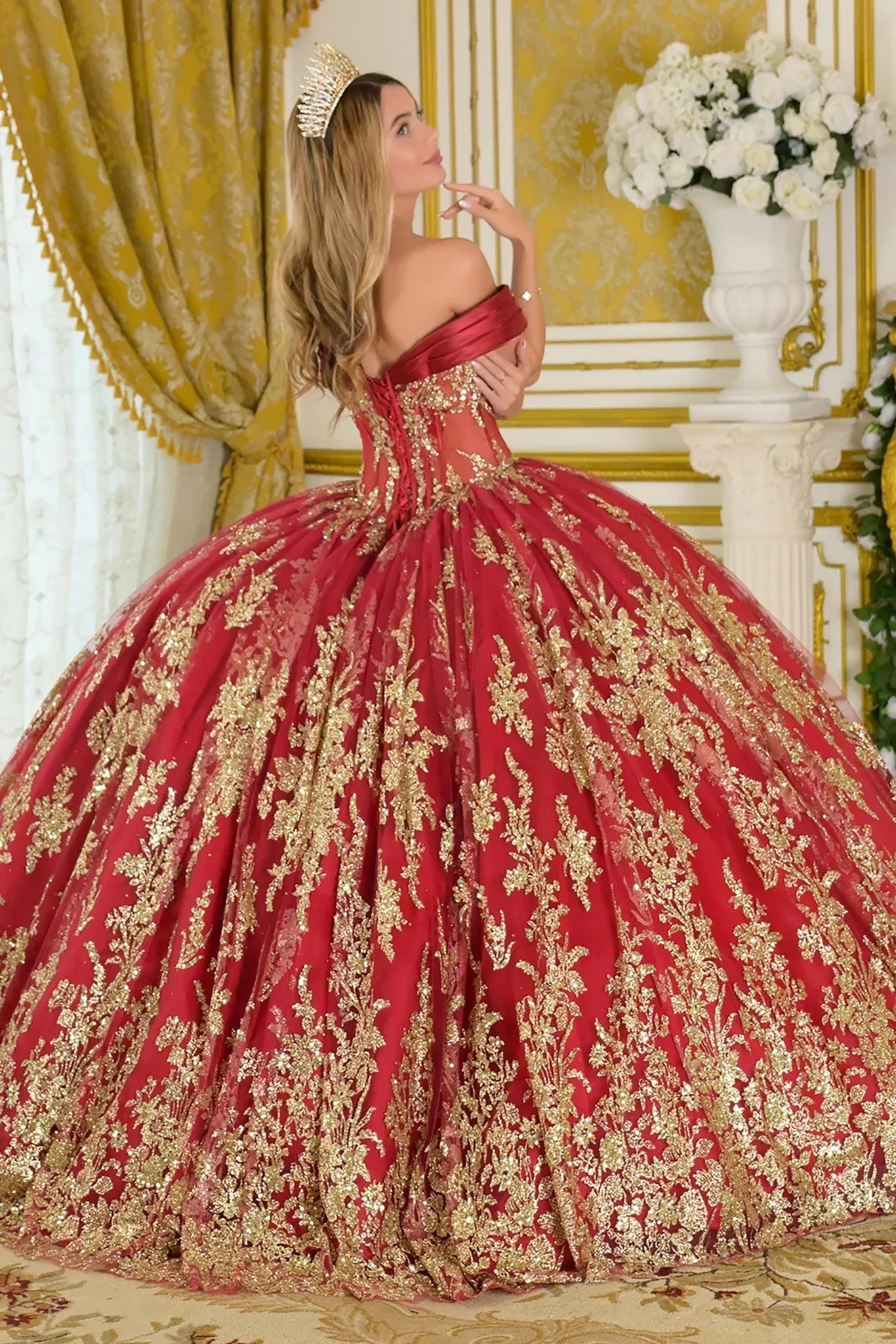 Woman wearing a red and gold quincenera ball gown in an elegant room.