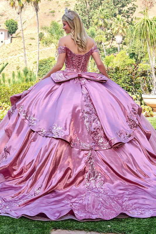 Woman in a dusty rose ball gown with floral details outdoors.