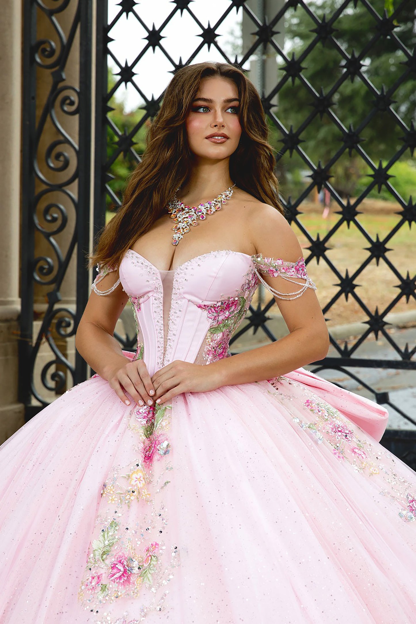 Woman in a pink floral dress standing in front of an ornate metal gate.