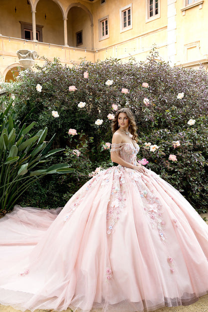 Woman in a pink floral gown standing in a garden with flowers and a building in the background