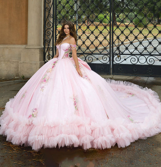 Pink ball gown with floral details worn by a model in front of an ornate gate.