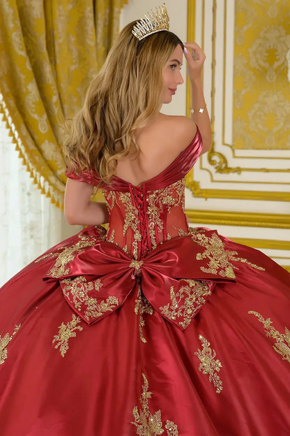Woman in a burgundy ball gown with gold embroidery and a tiara, standing in a decorated room.