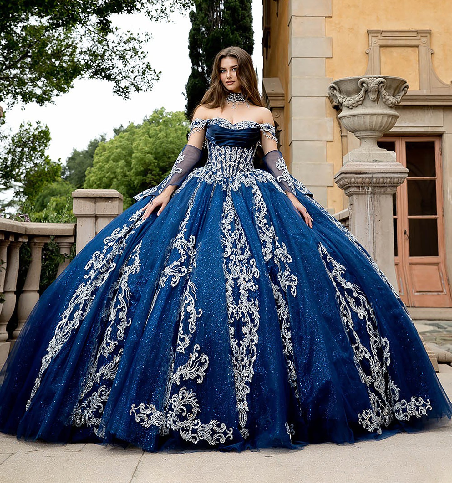 Woman in a blue ball gown with silver embroidery standing in front of a classical building.