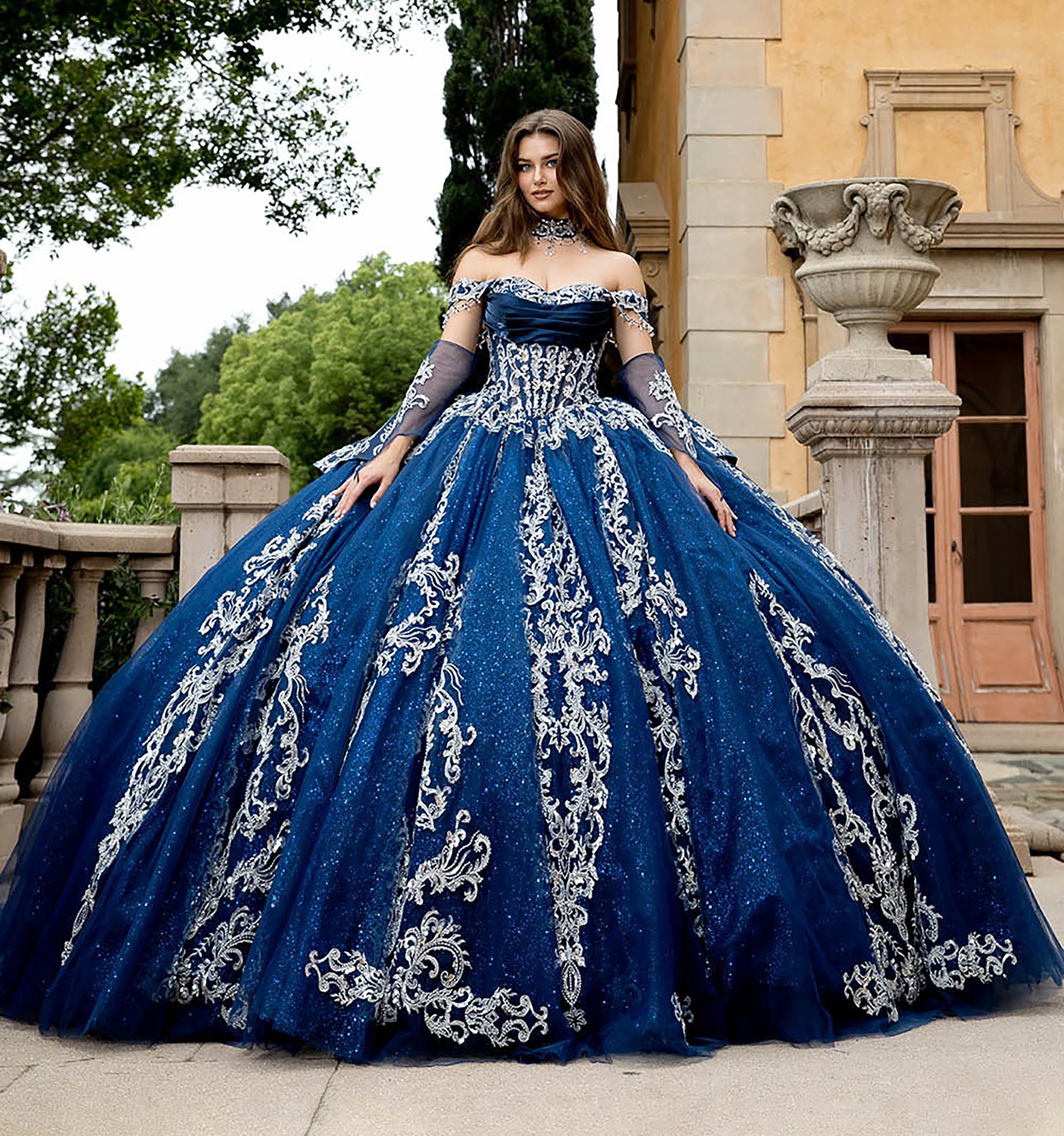 Woman in a blue ball gown with silver embroidery standing in front of a classical building.