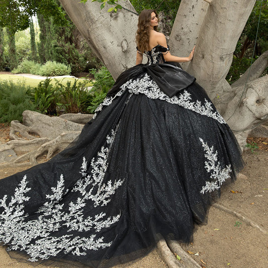 Woman in a black gown with white embroidery standing in a natural setting.