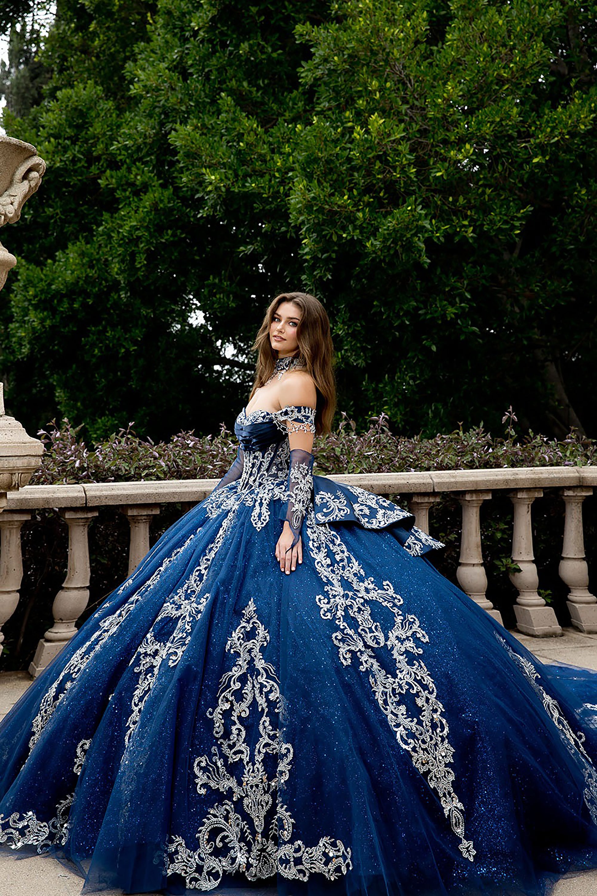 Woman in a blue ball gown with intricate designs standing outdoors.