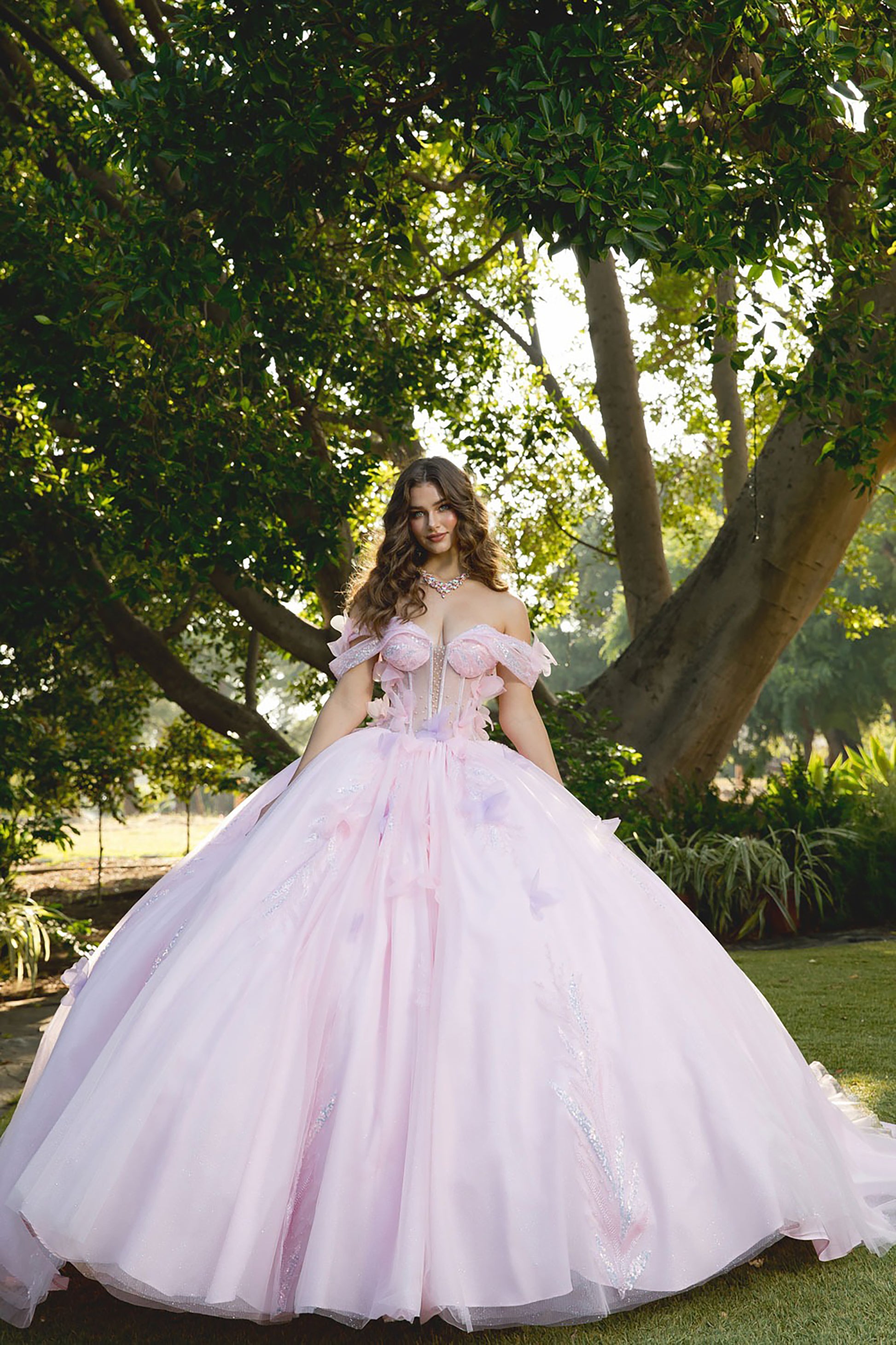 Woman in a pink gown standing in a garden with trees and greenery.