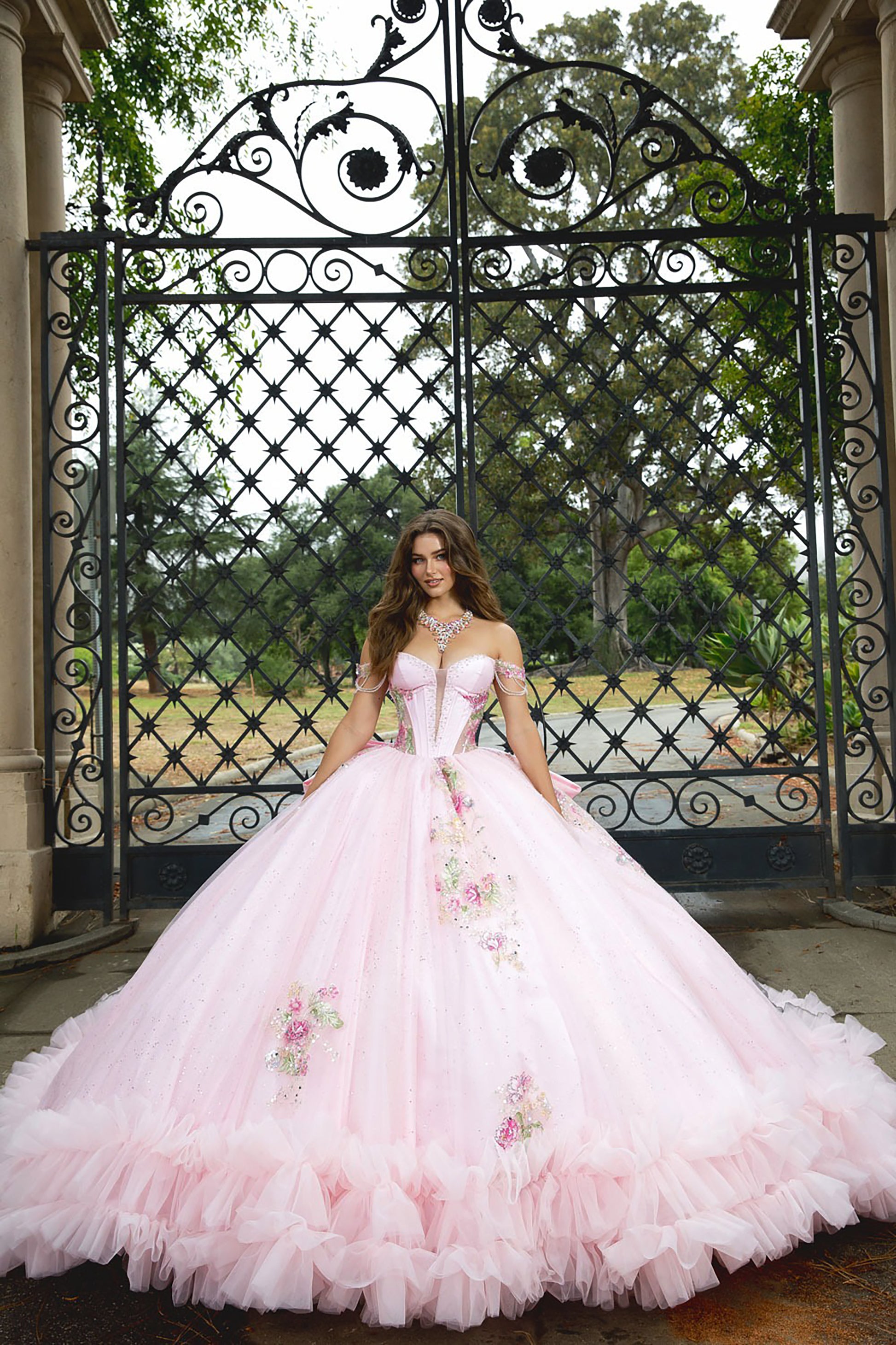 Woman in a pink floral dress standing in front of an ornate metal gate.