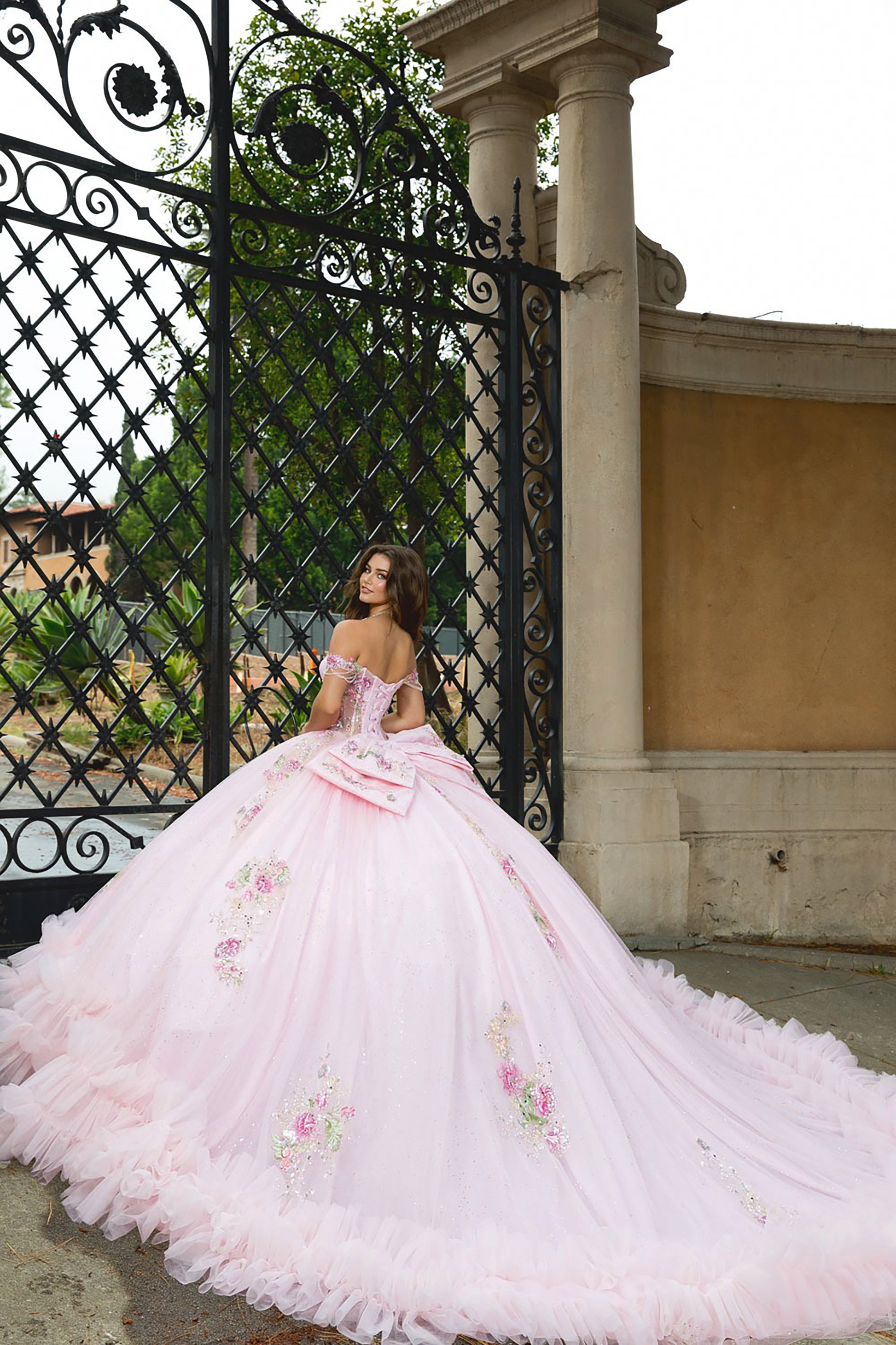 Woman in a pink floral dress standing in front of an ornate gate.