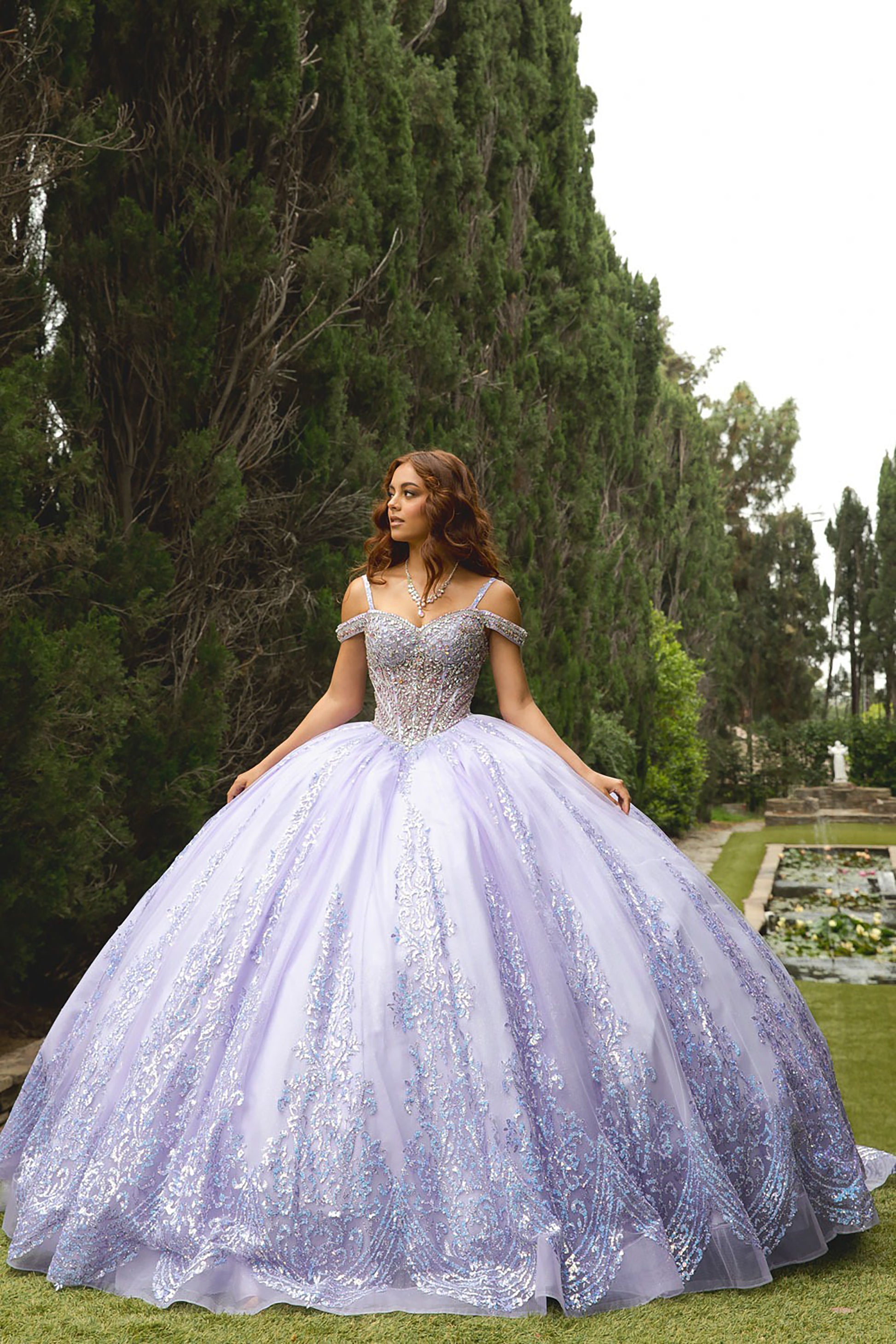 Woman in a purple embroidered gown standing in a garden with trees and grass.