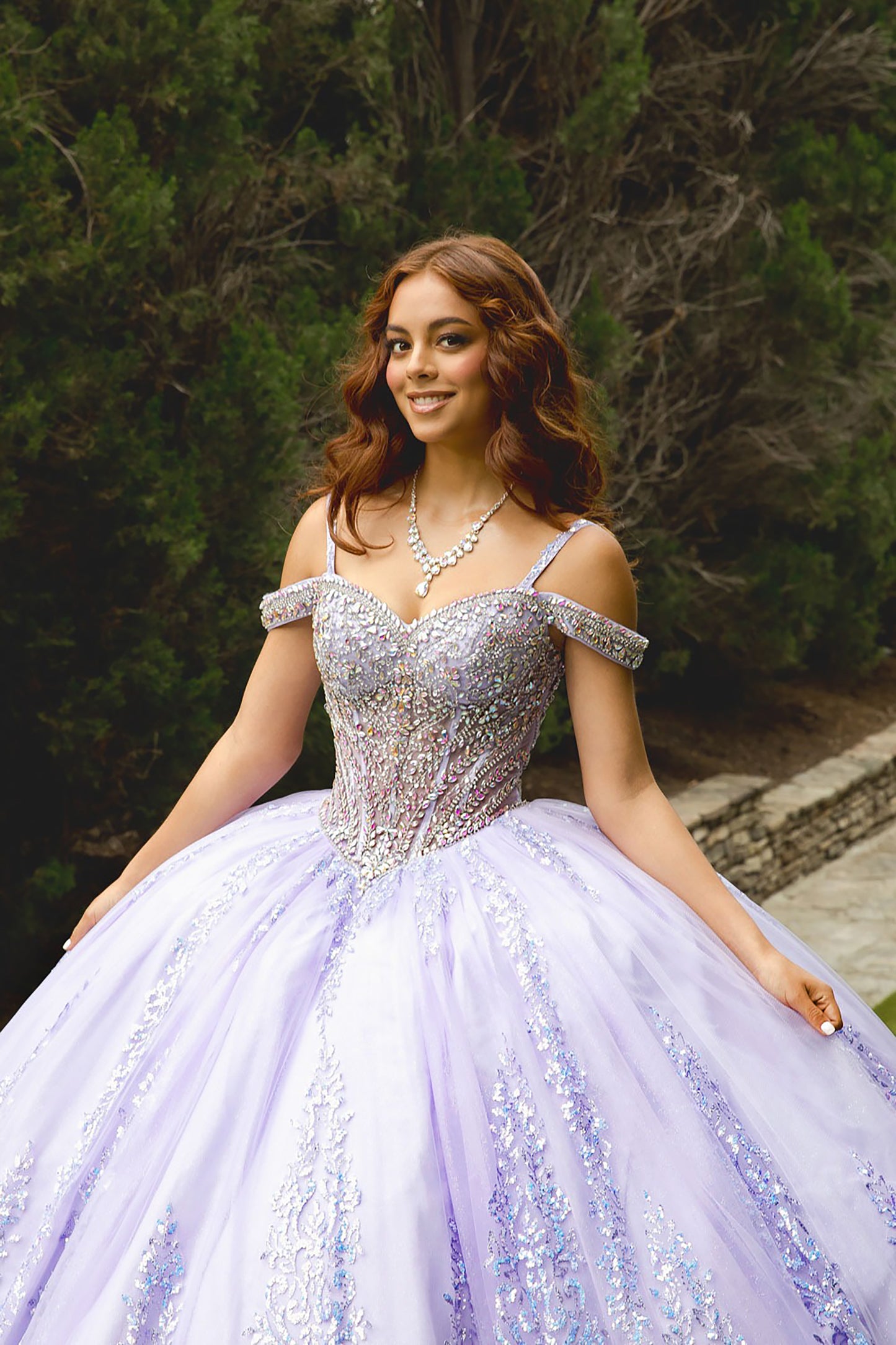 Woman in a sparkling purple gown sitting outdoors with greenery in the background