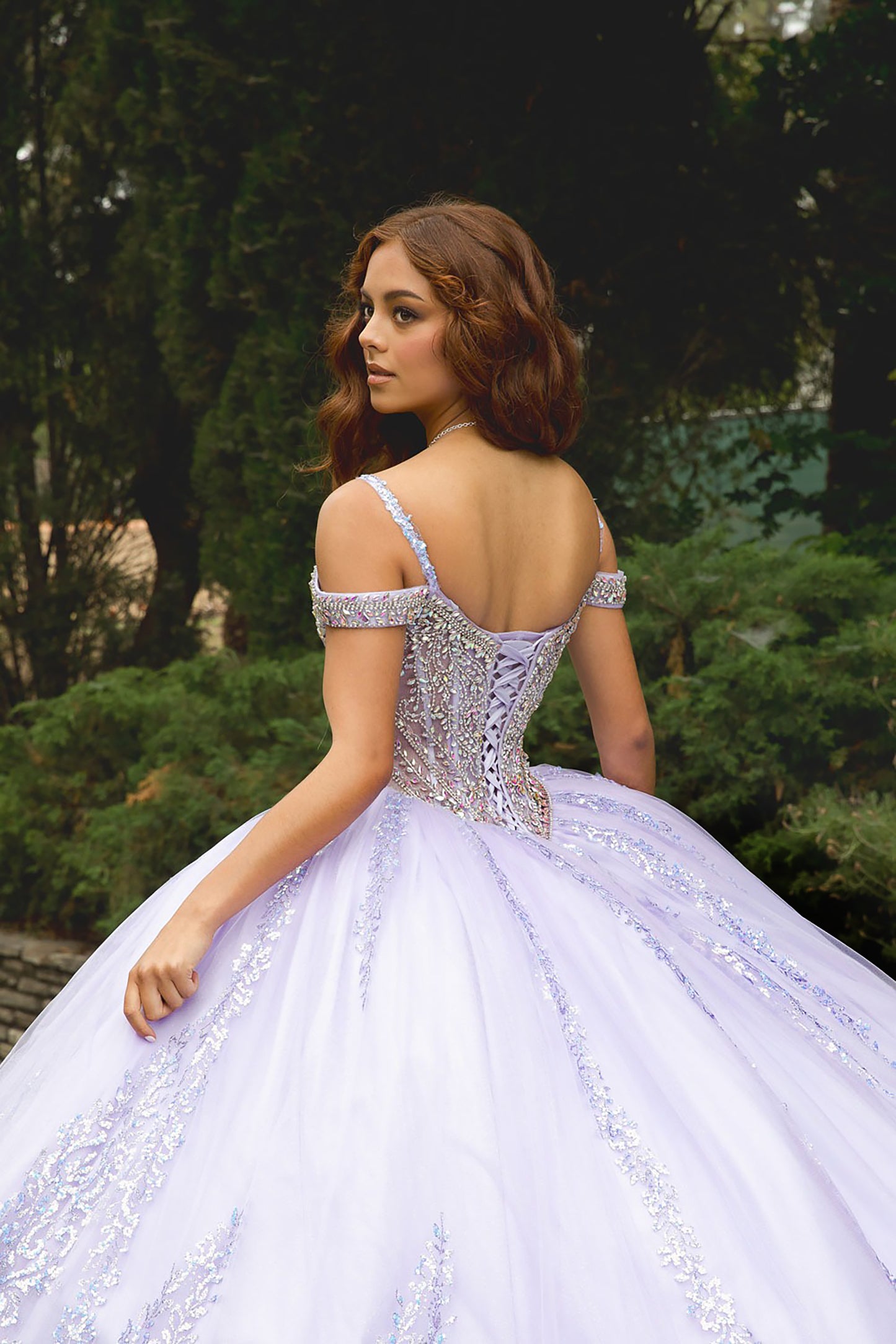 Woman in a white, off-shoulder gown with intricate detailing standing outdoors.