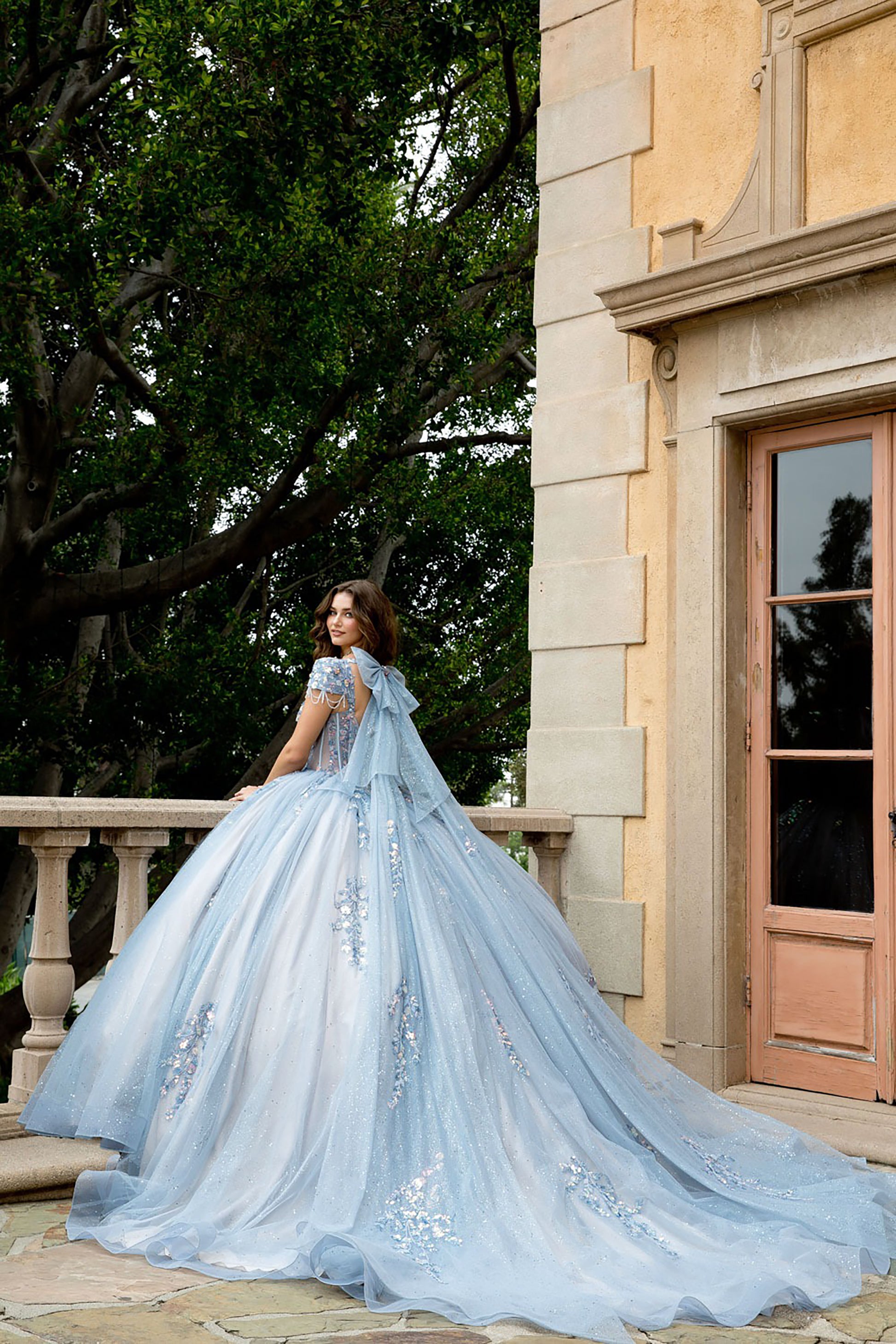 Woman in a light blue wedding dress standing in front of a stone building with trees in the background