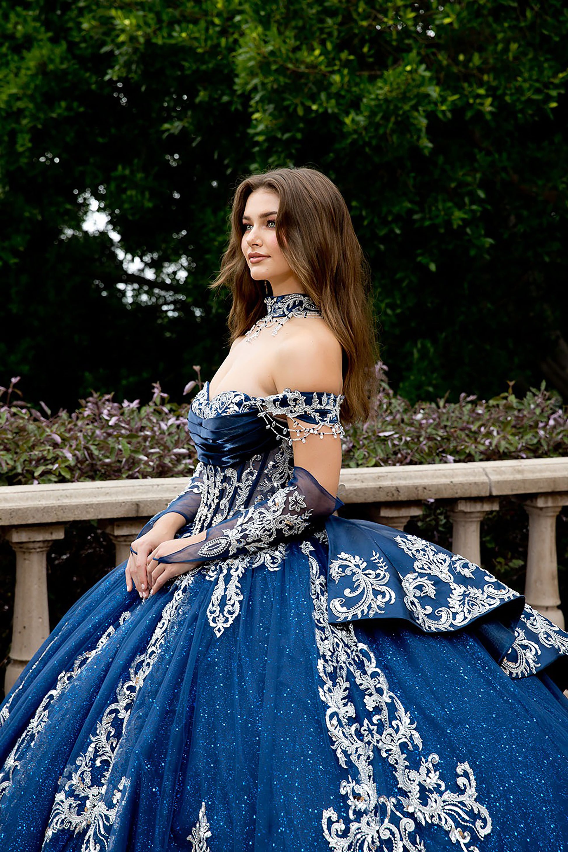 Woman in a blue and white formal gown standing outdoors with greenery in the background