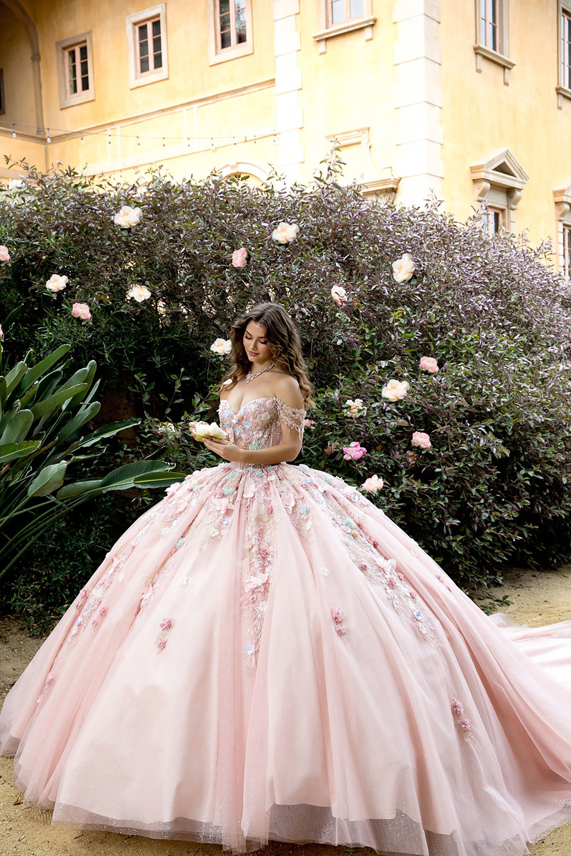 Woman in a pink floral dress standing in front of a building with flowers.
