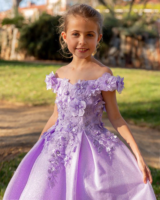 Young girl in a purple floral dress standing outdoors with greenery in the background