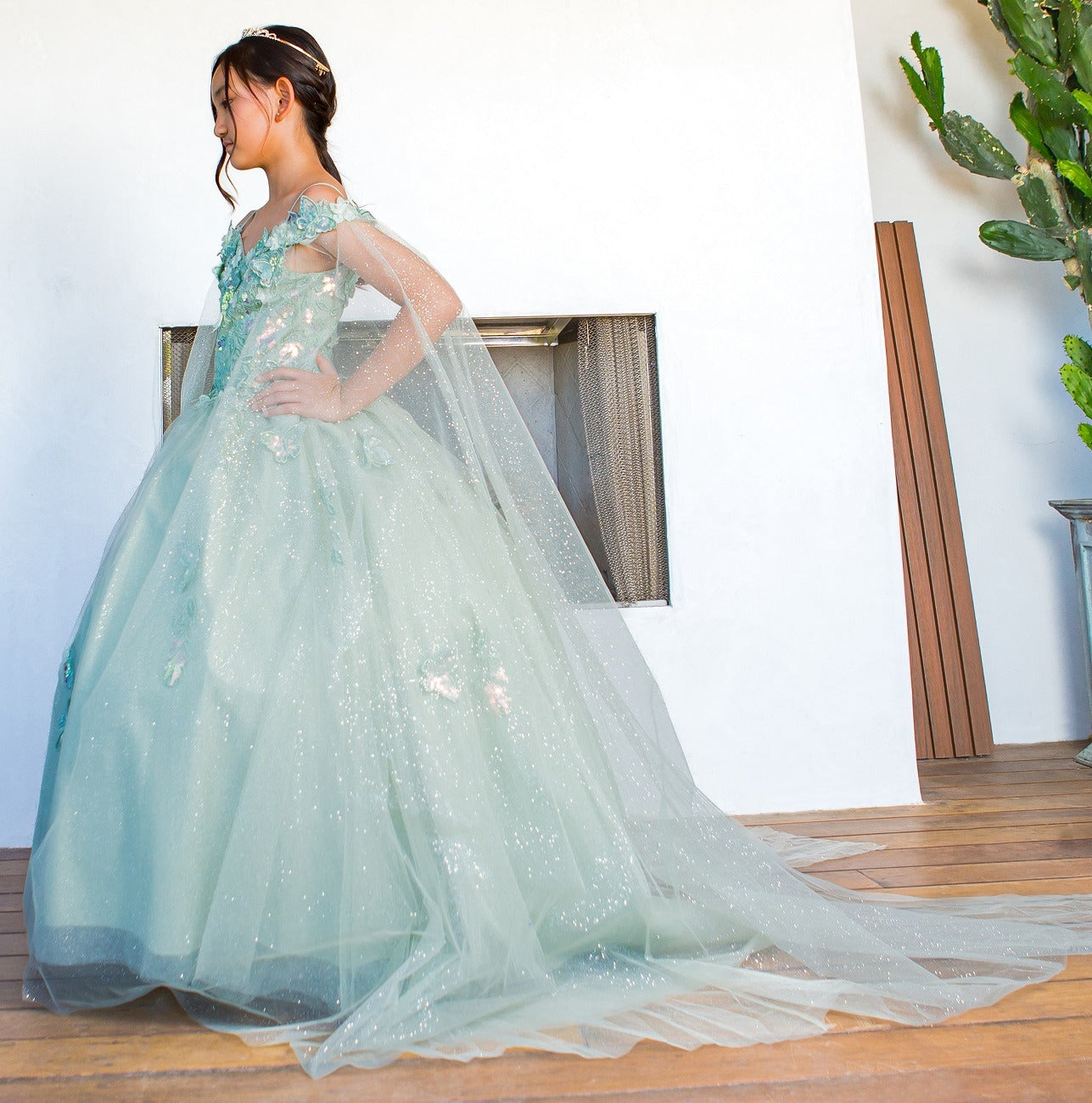 Young girl in a light blue sparkly dress standing indoors.