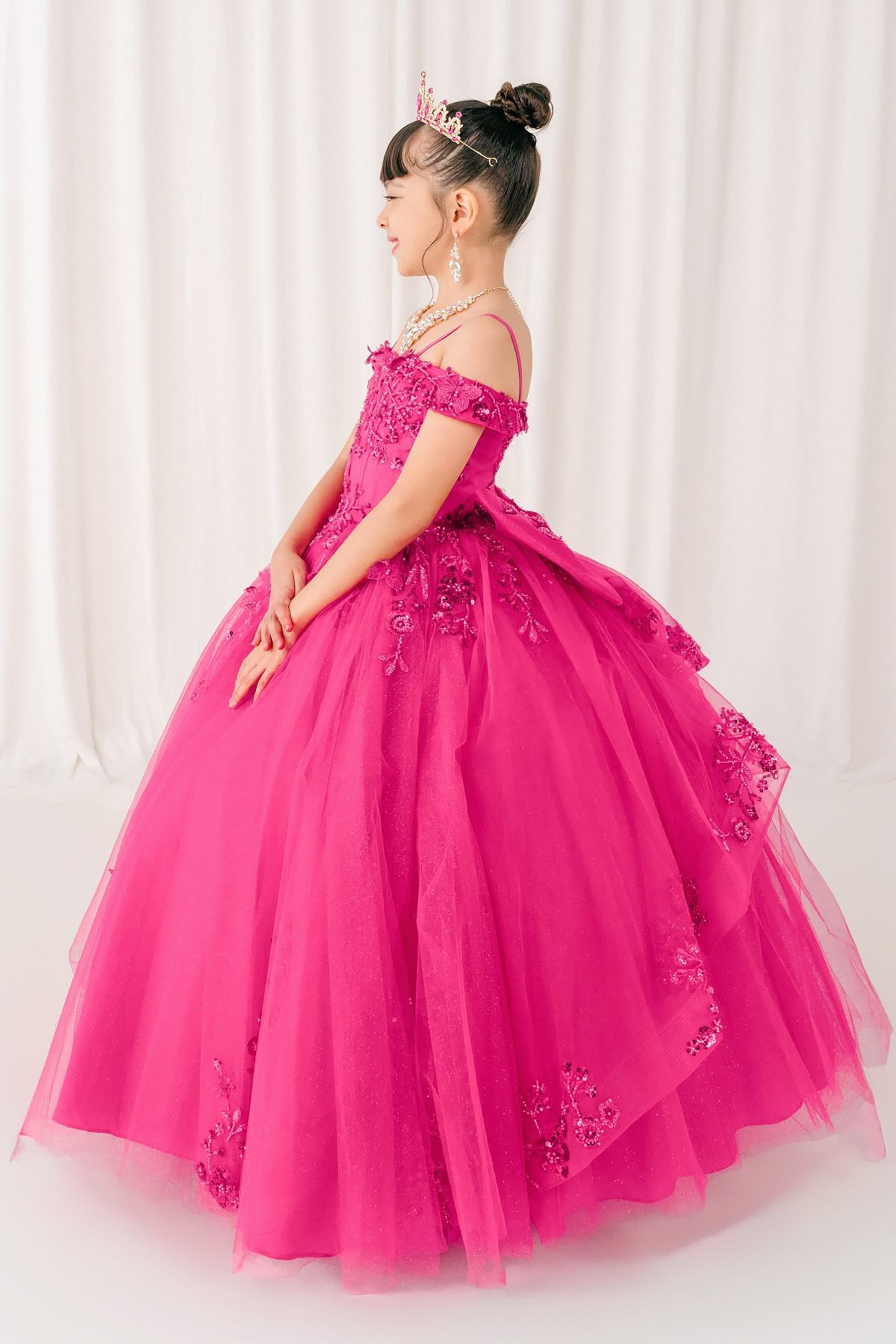 kid in a fuchsia formal mini quince gown with floral details against a white curtain background