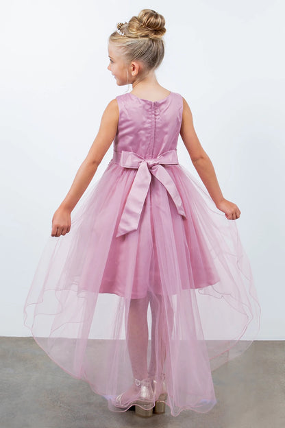 Young girl standing back-facing in dusty rose sleeveless high-low tulle flower girl dress with lace-up closure, pearl trim neckline, rhinestone details, and cascading skirt