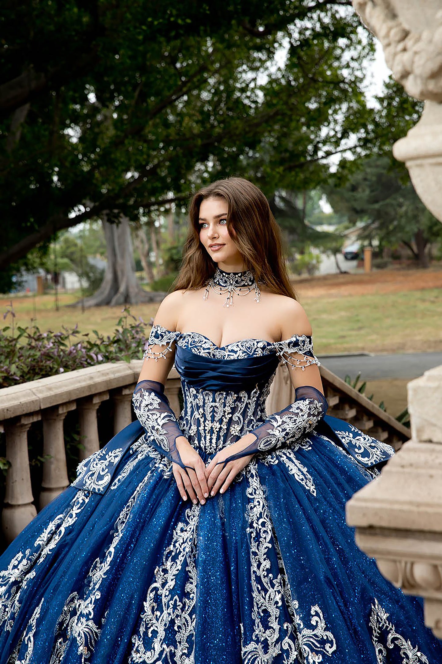 Woman in a blue and white embroidered gown standing outdoors.