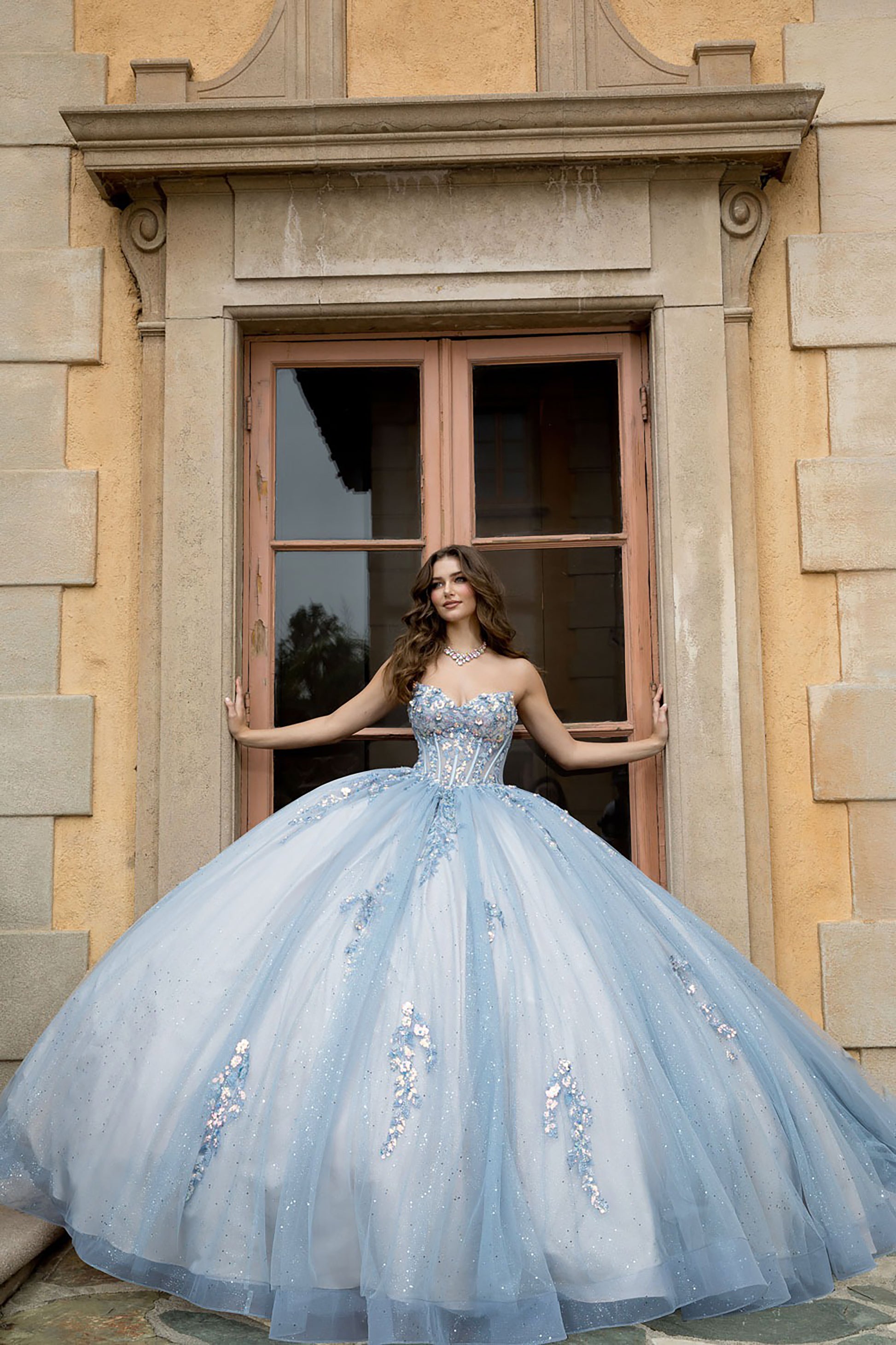 Woman in a blue gown standing in front of a stone building with large windows.
