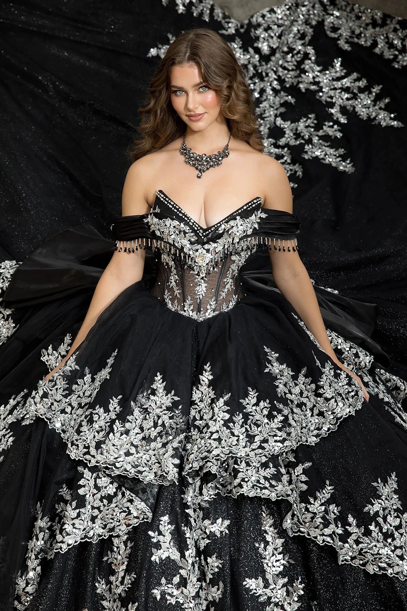 Woman in a v neck black and silver embroidery ball gown standing in front of a large tree