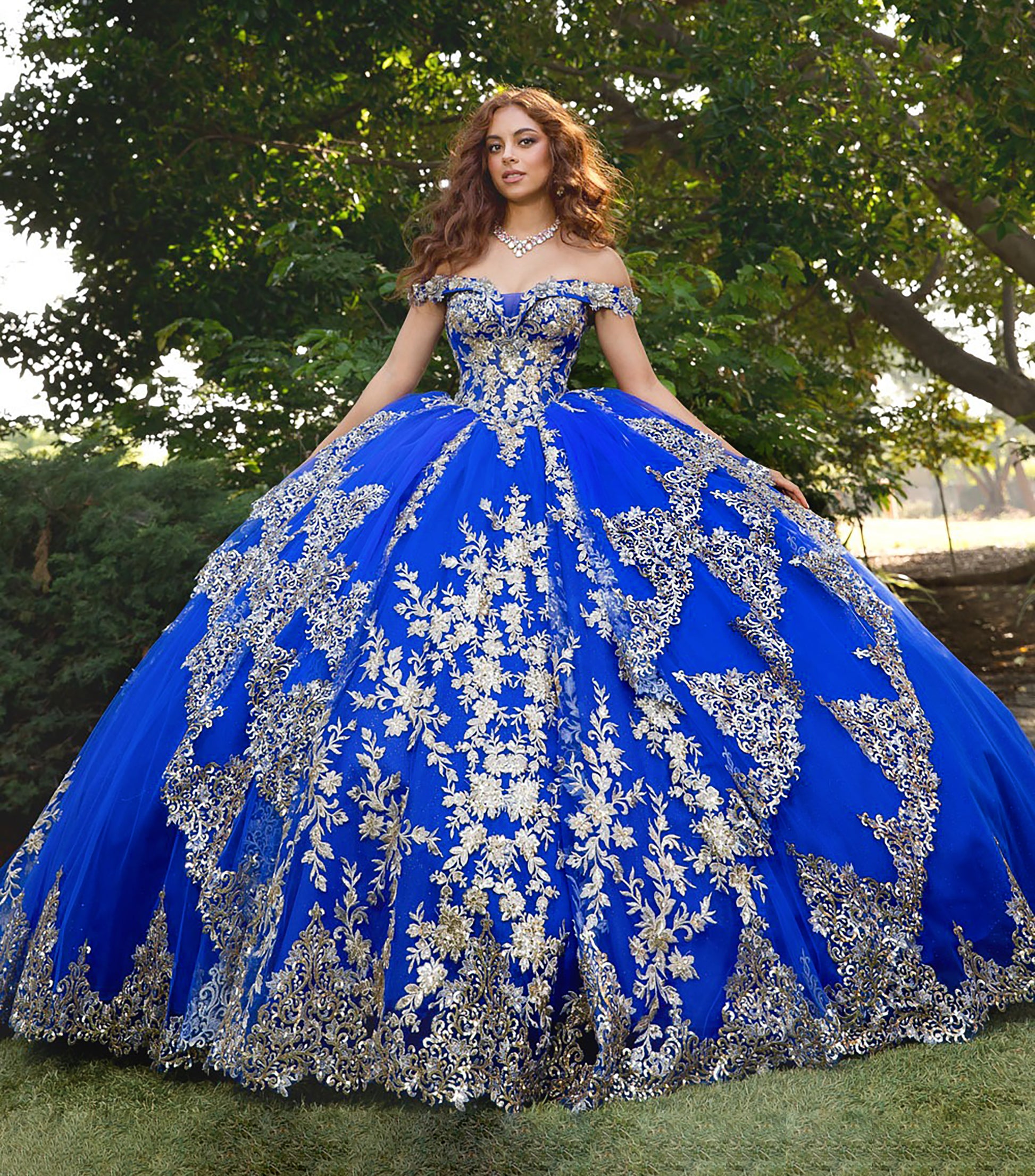 Woman wearing a blue and silver ball gown with floral patterns outdoors.